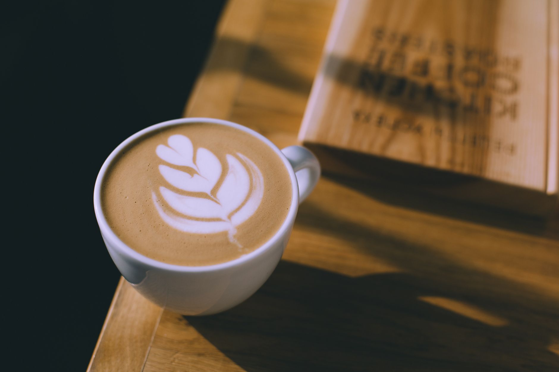 From above of ceramic cup with hot late with decorative leaf on foam in cafe