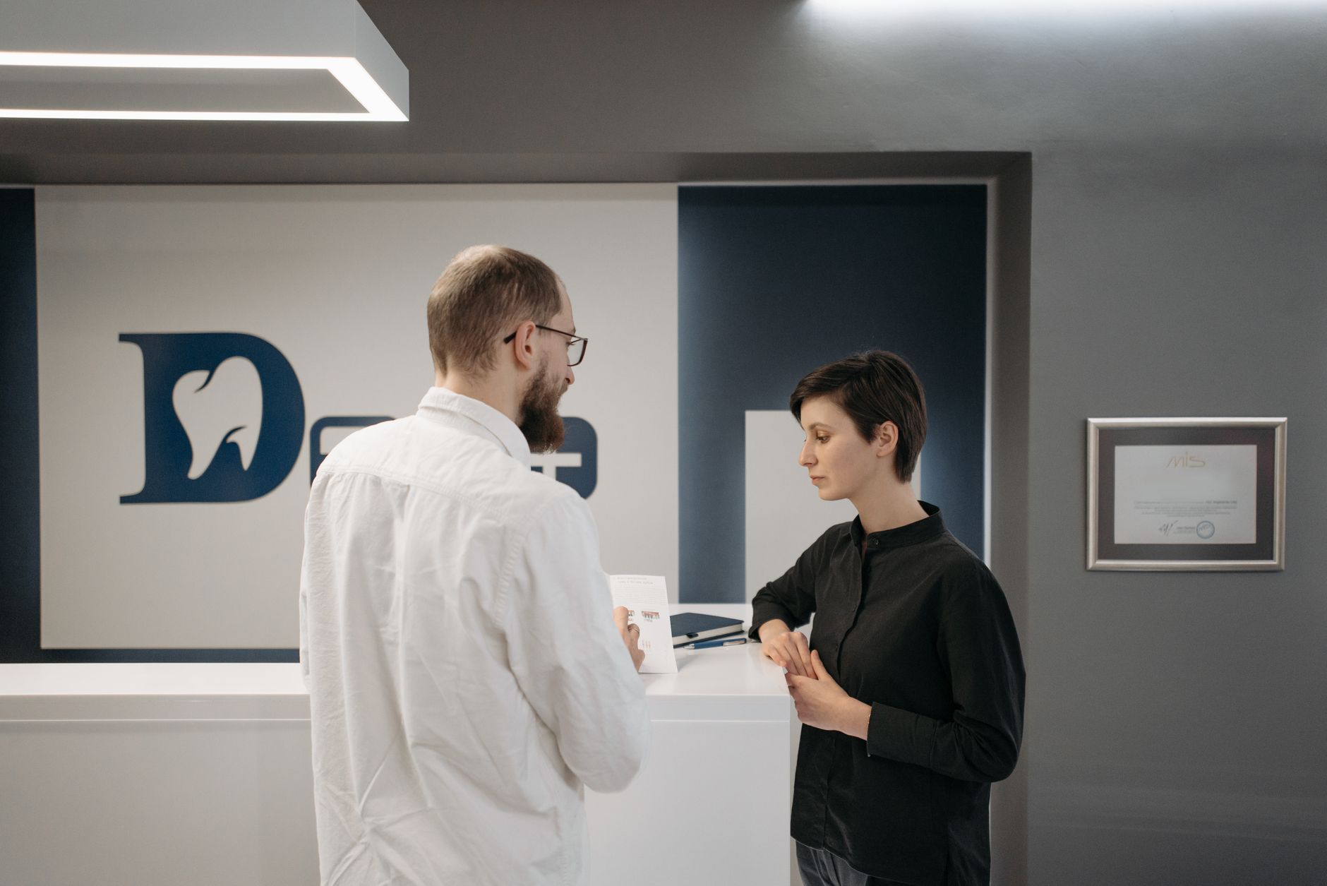A male dentist consulting a female patient at a modern dental clinic reception.