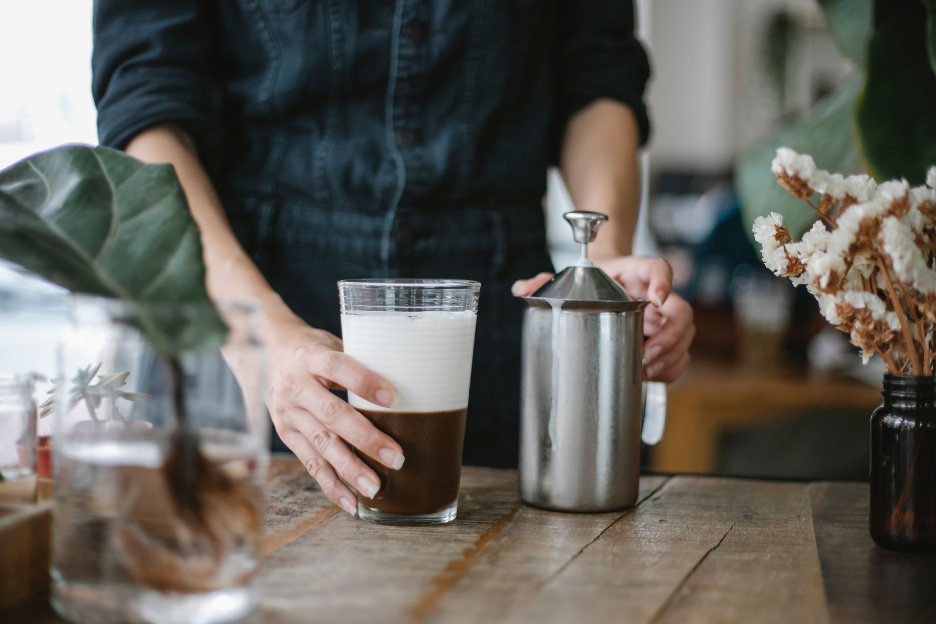 Crop unrecognizable female barista touching manual milk frother and preparing iced chocolate coffee at table in cafe