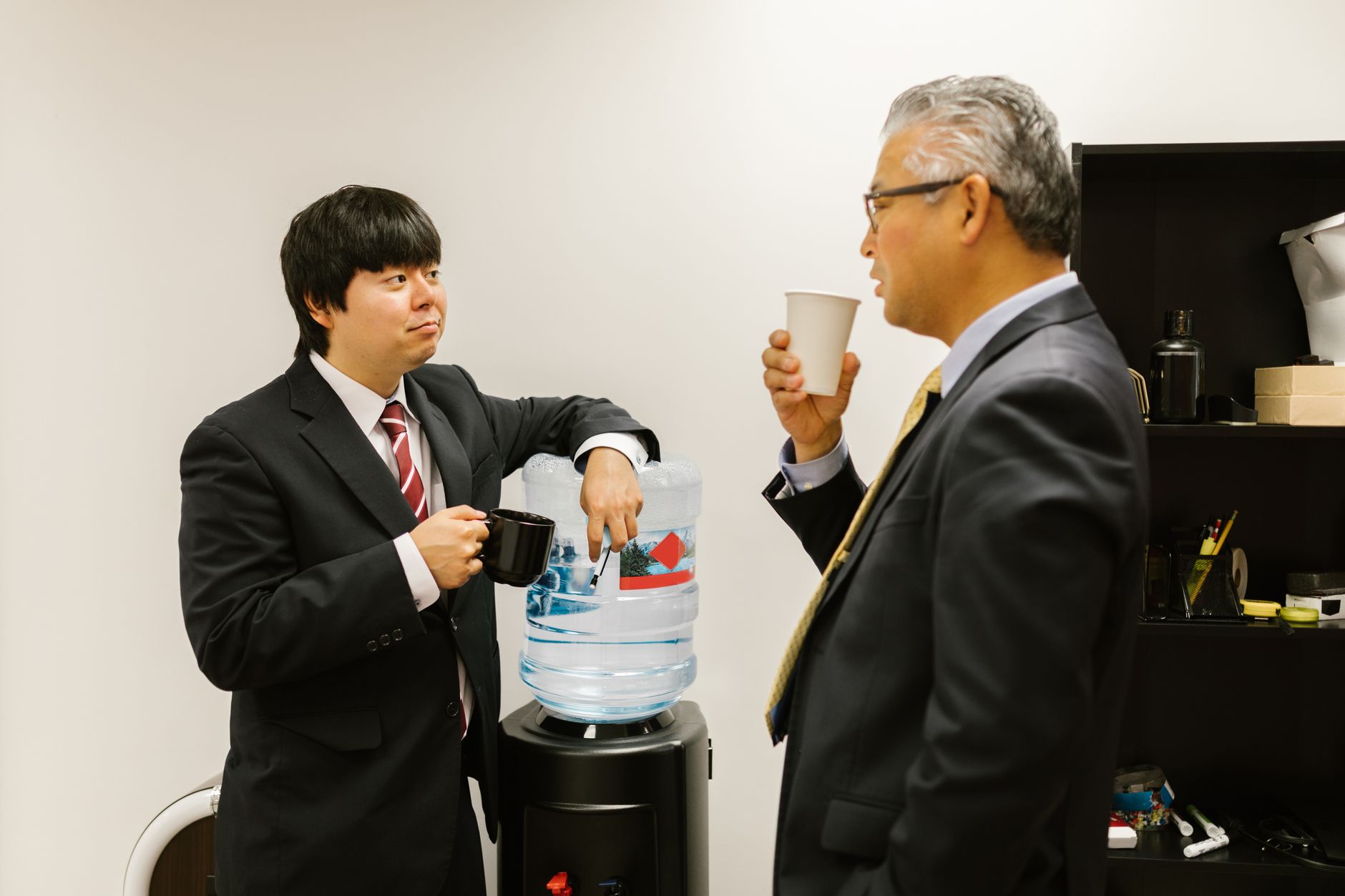 Two businessmen in suits chatting by a water cooler, representing casual teamwork.