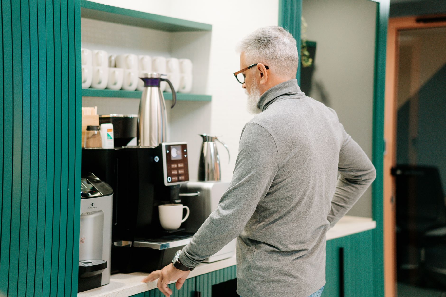 Elderly man in gray sweater making coffee indoors with a modern machine.