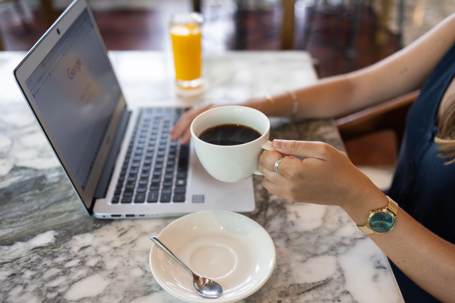 A woman in a café working on a laptop, holding a cup of black coffee, creating a productive atmosphere.