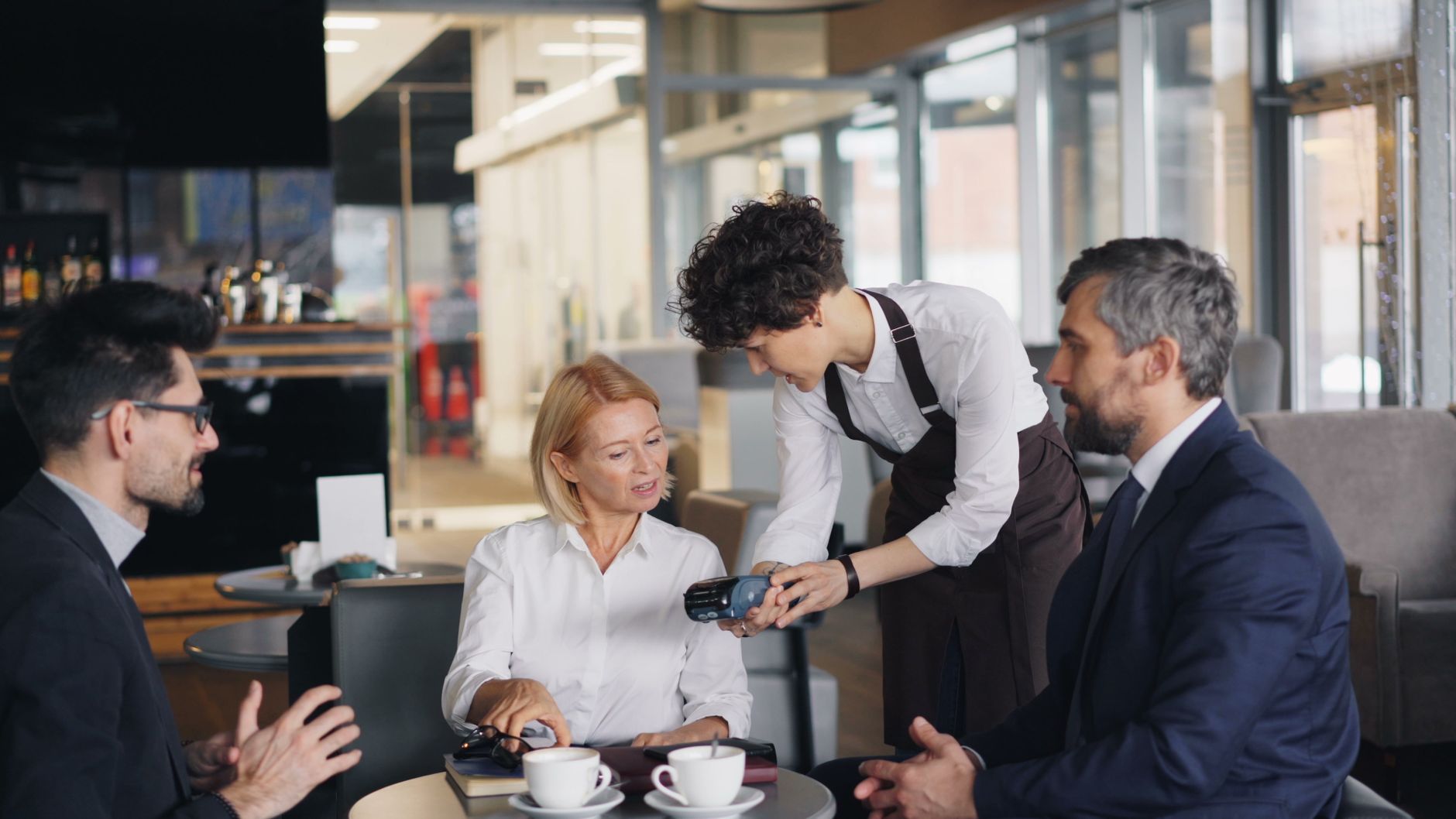Professionals in a cafe discussing business while making a payment.