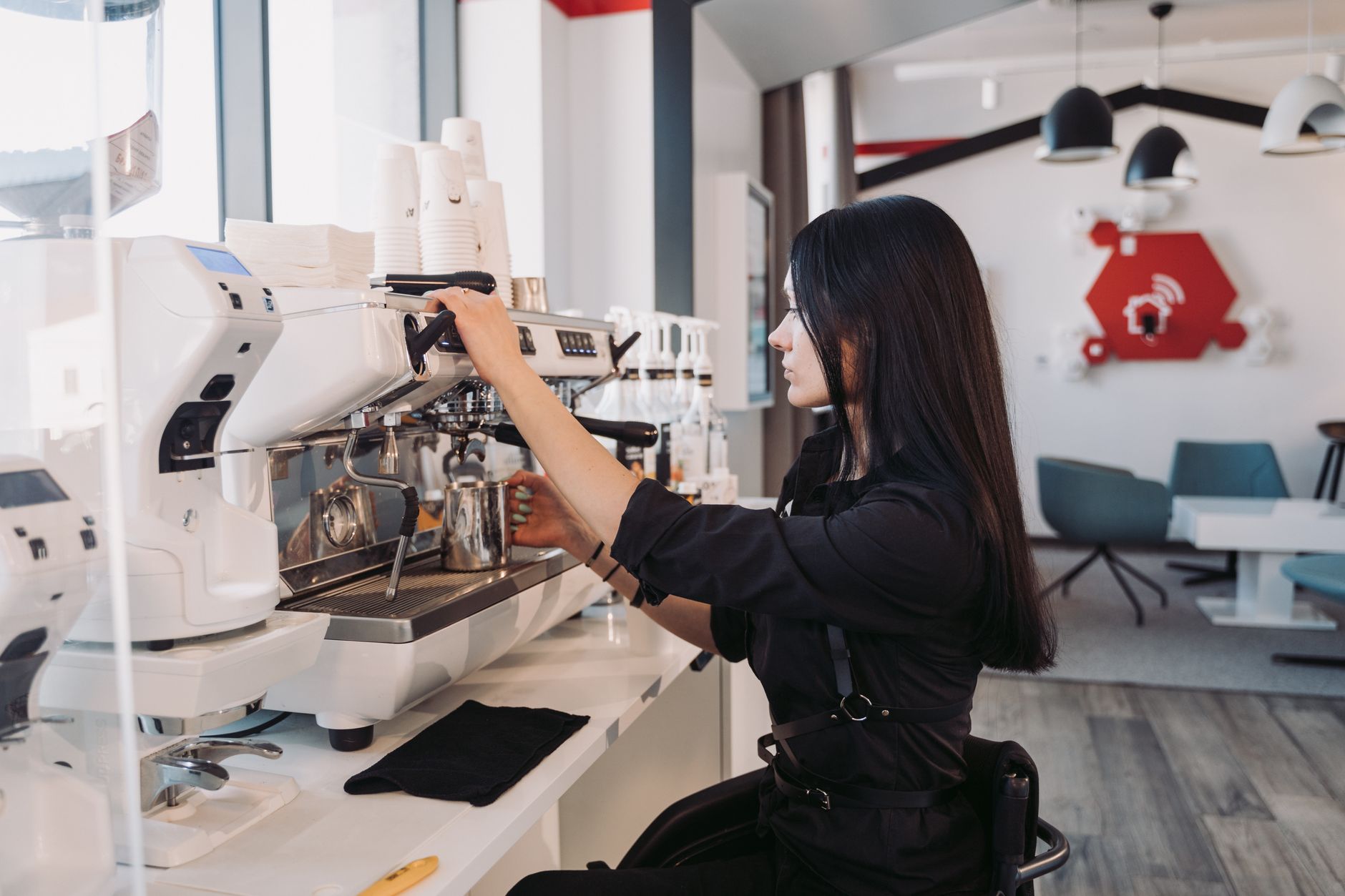 Woman barista operates espresso machine in contemporary café interior.
