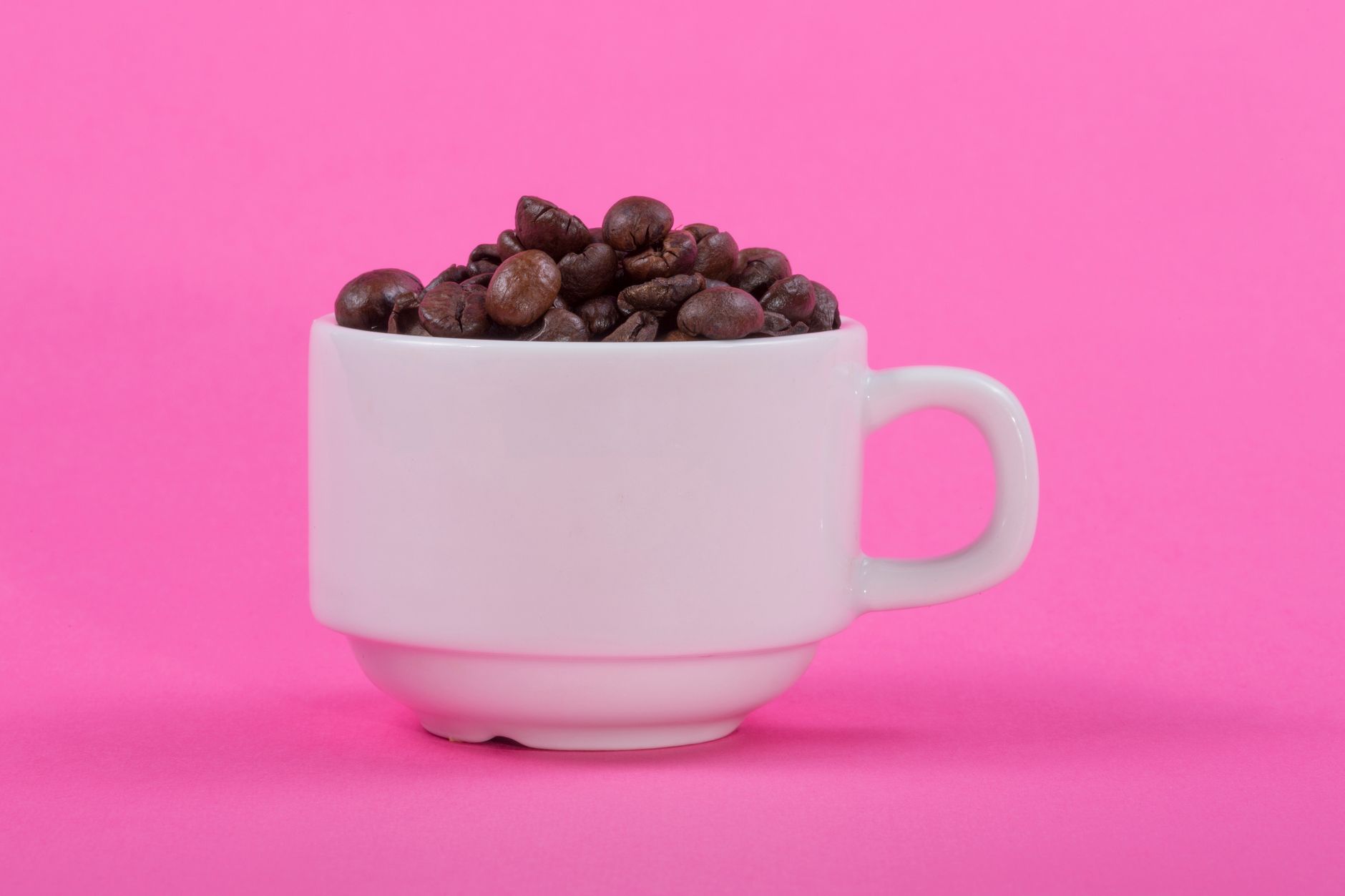 Aesthetic coffee cup filled with beans on a vibrant pink backdrop, ideal for cafe promotions.