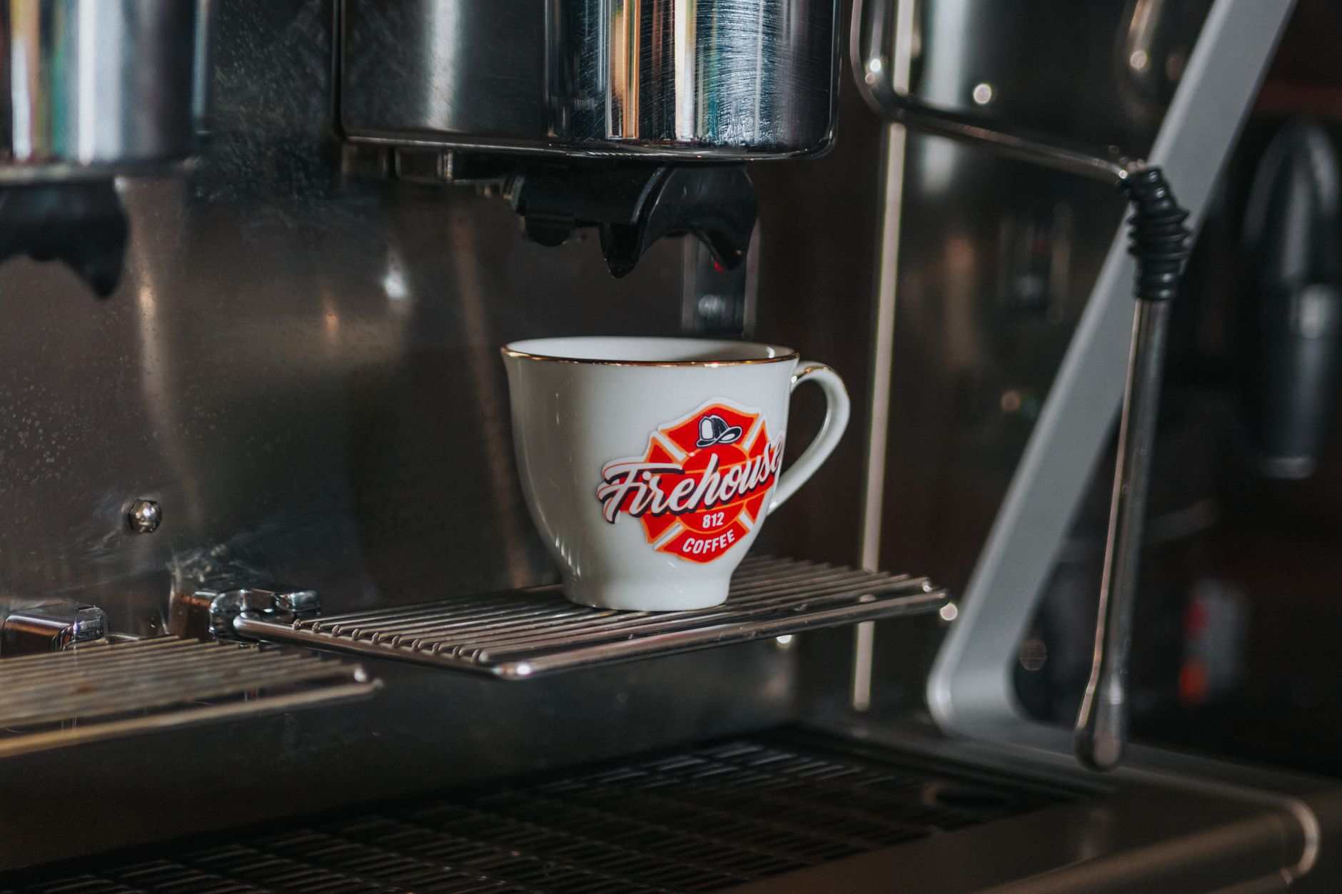 A coffee cup with Firehouse branding under an espresso machine, ready to brew.