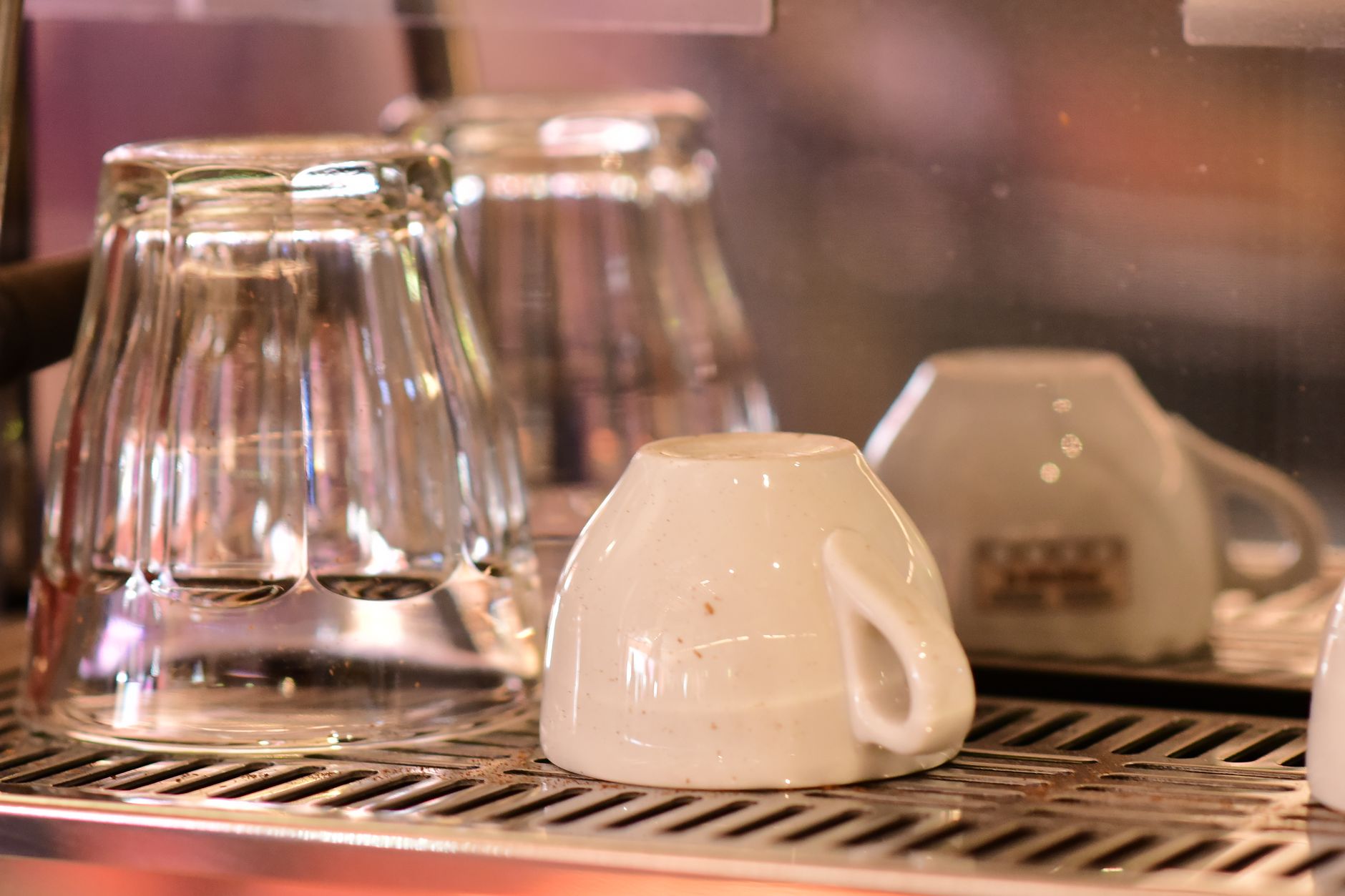Close-up of an upside-down coffee cup and glass tumblers drying on an espresso machine drip tray.
