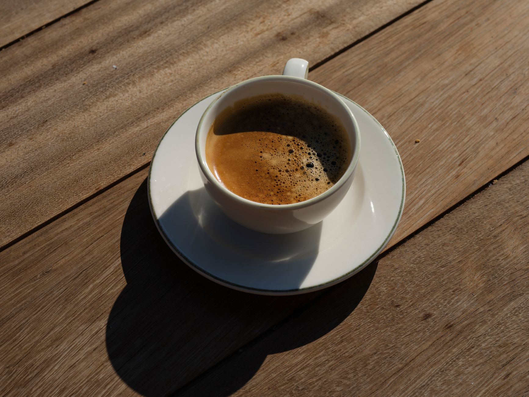 Top view of a steaming espresso in white cup on rustic wooden table.