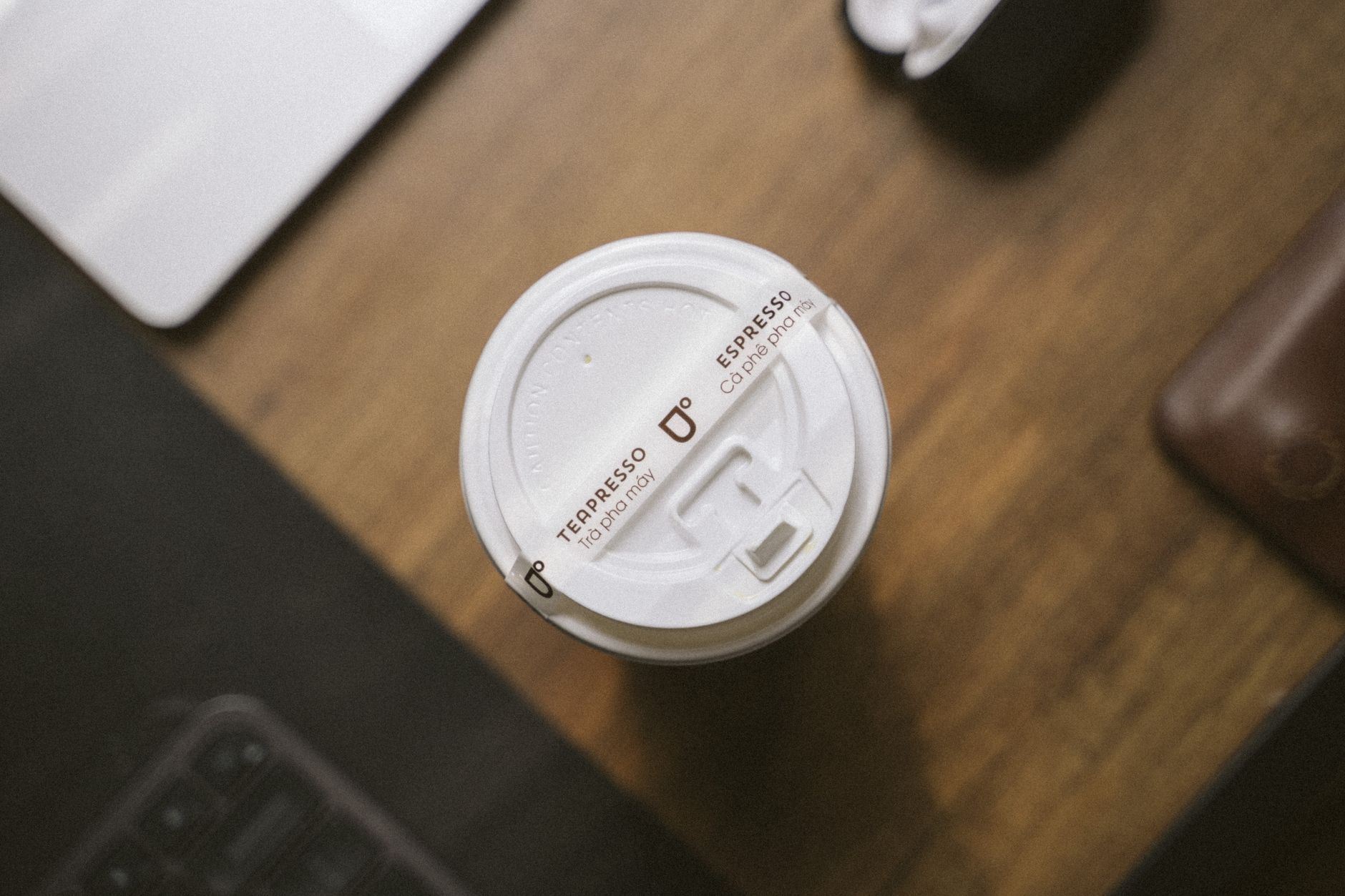 Disposable coffee cup with plastic lid on a wooden desk, top view.