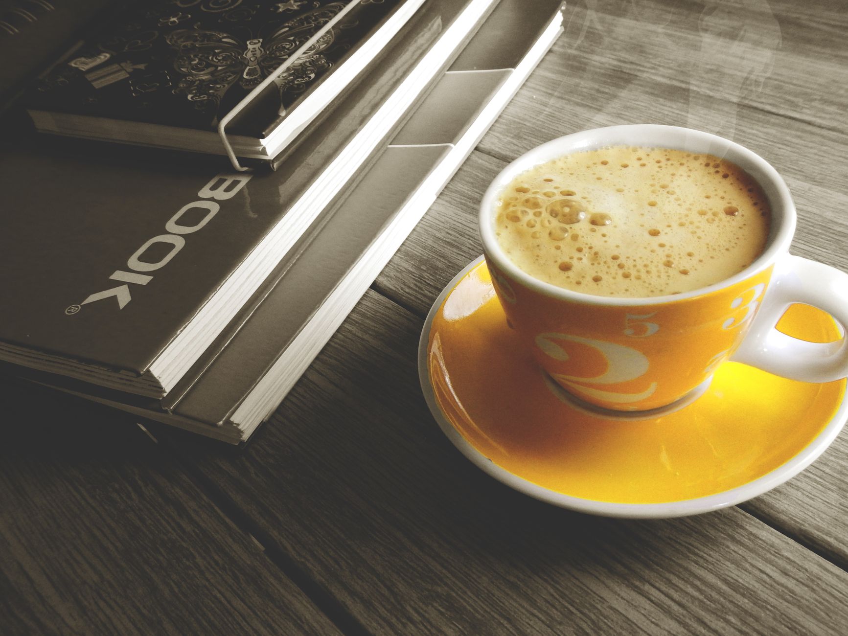 A warm cup of coffee on a yellow saucer beside a stack of books, perfect for a relaxing break.