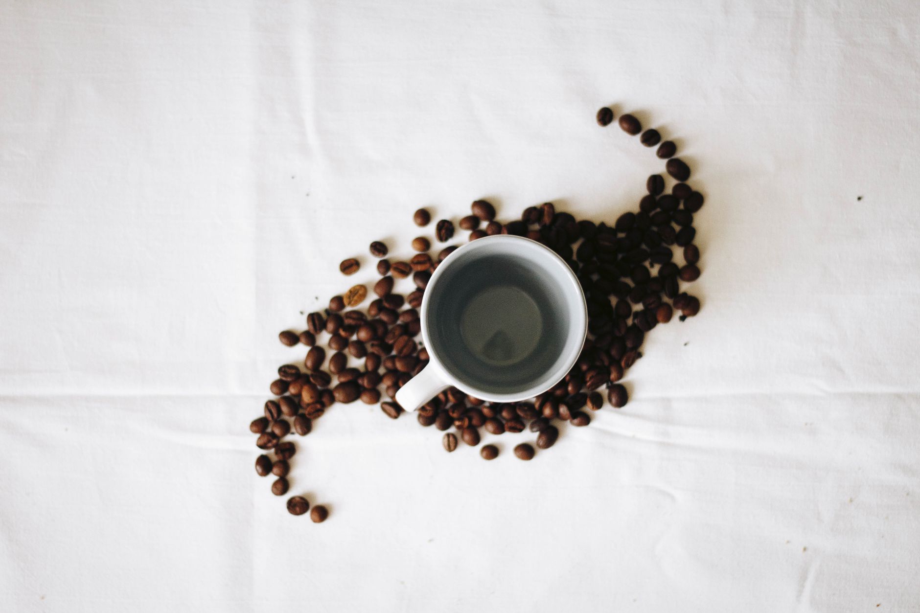 A minimalist flat lay of coffee beans surrounding an empty coffee mug on a white background.