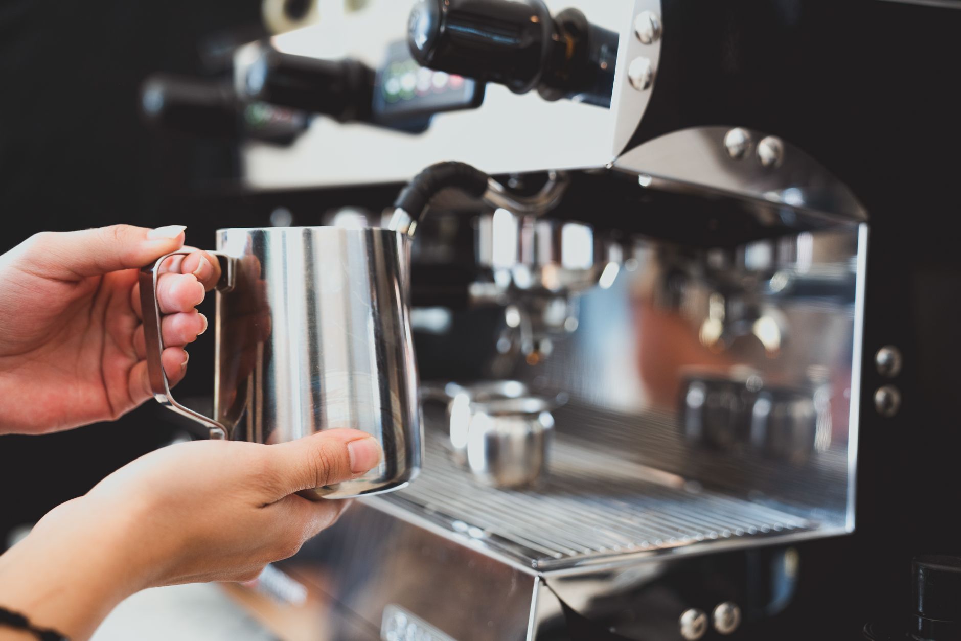 Close-up of barista using espresso machine to steam milk in a coffee shop.