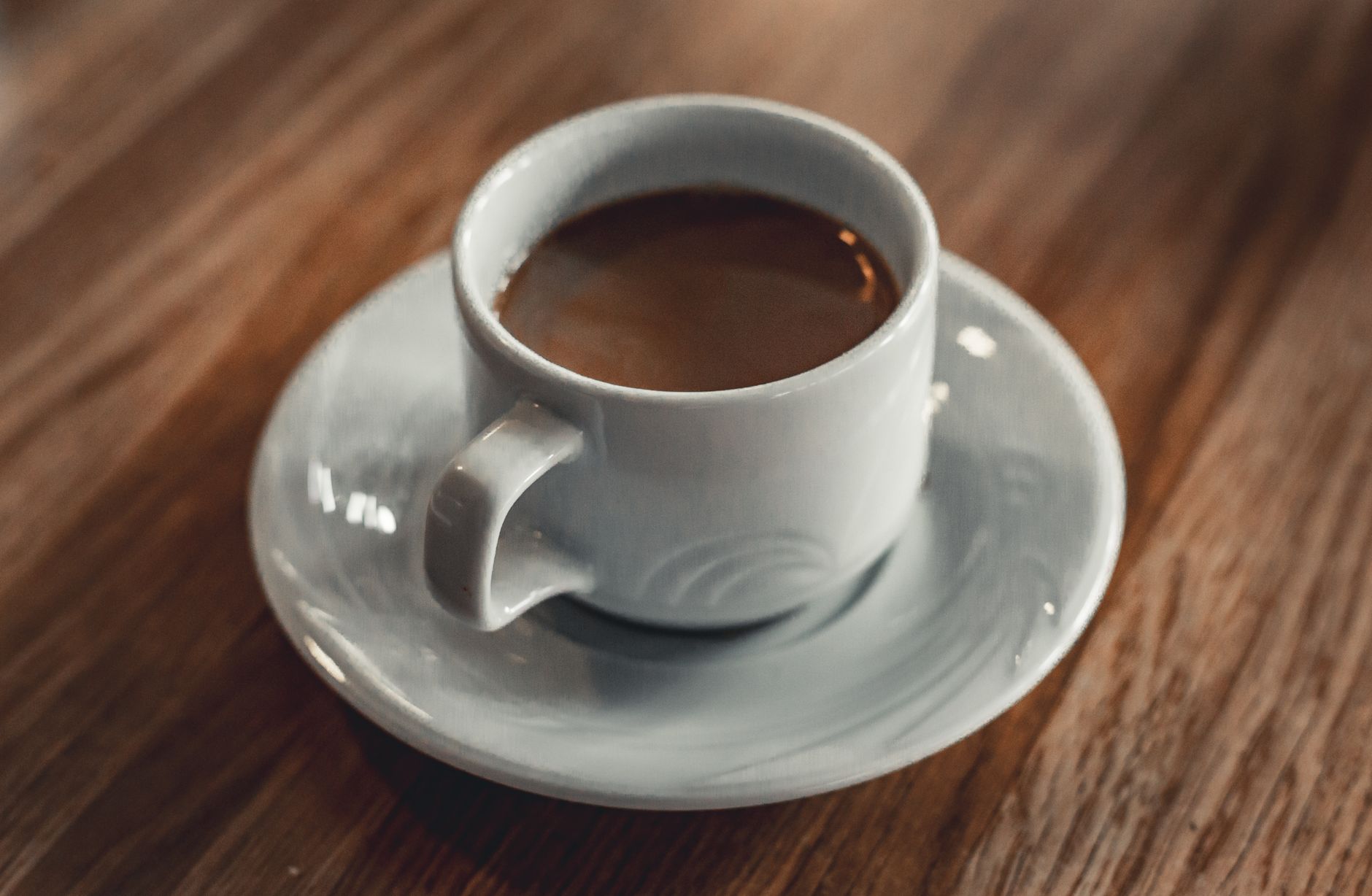 A warm cup of coffee in a white mug placed on a wooden table, creating a cozy atmosphere.