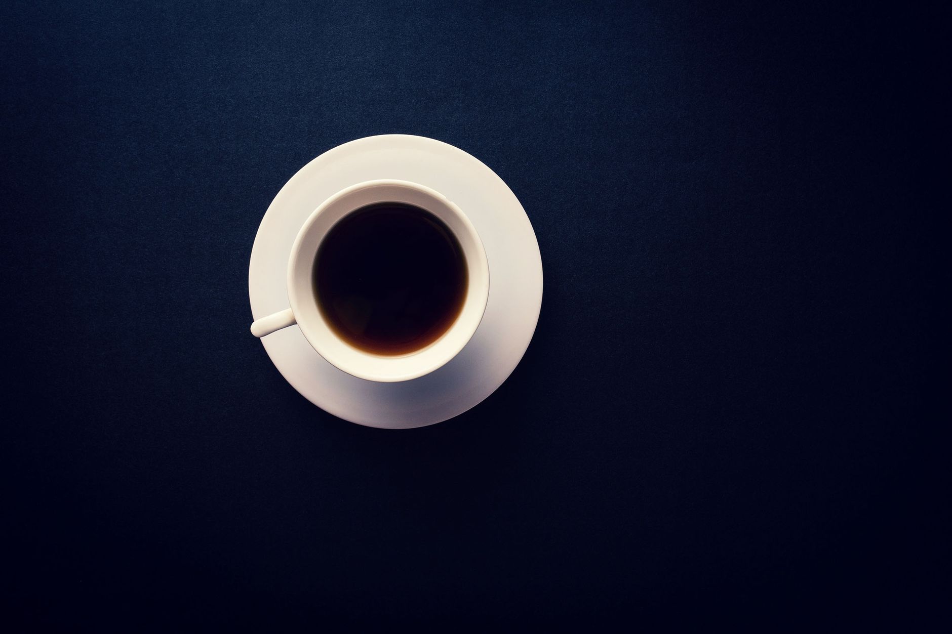 A minimalist overhead shot of a black coffee in a white cup on a dark background.