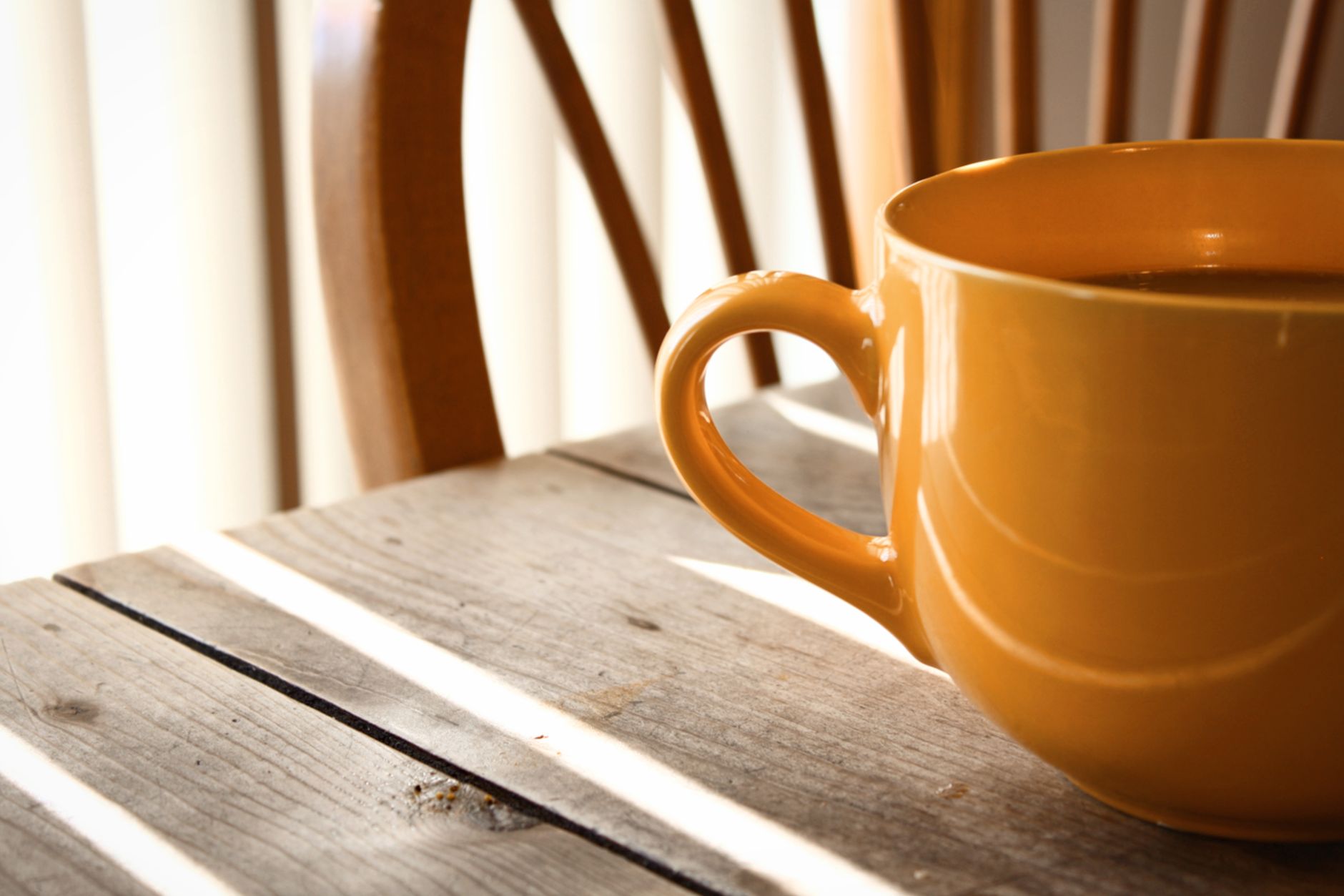 A close-up of a yellow coffee mug on a wooden table with warm sunlight streaming in.