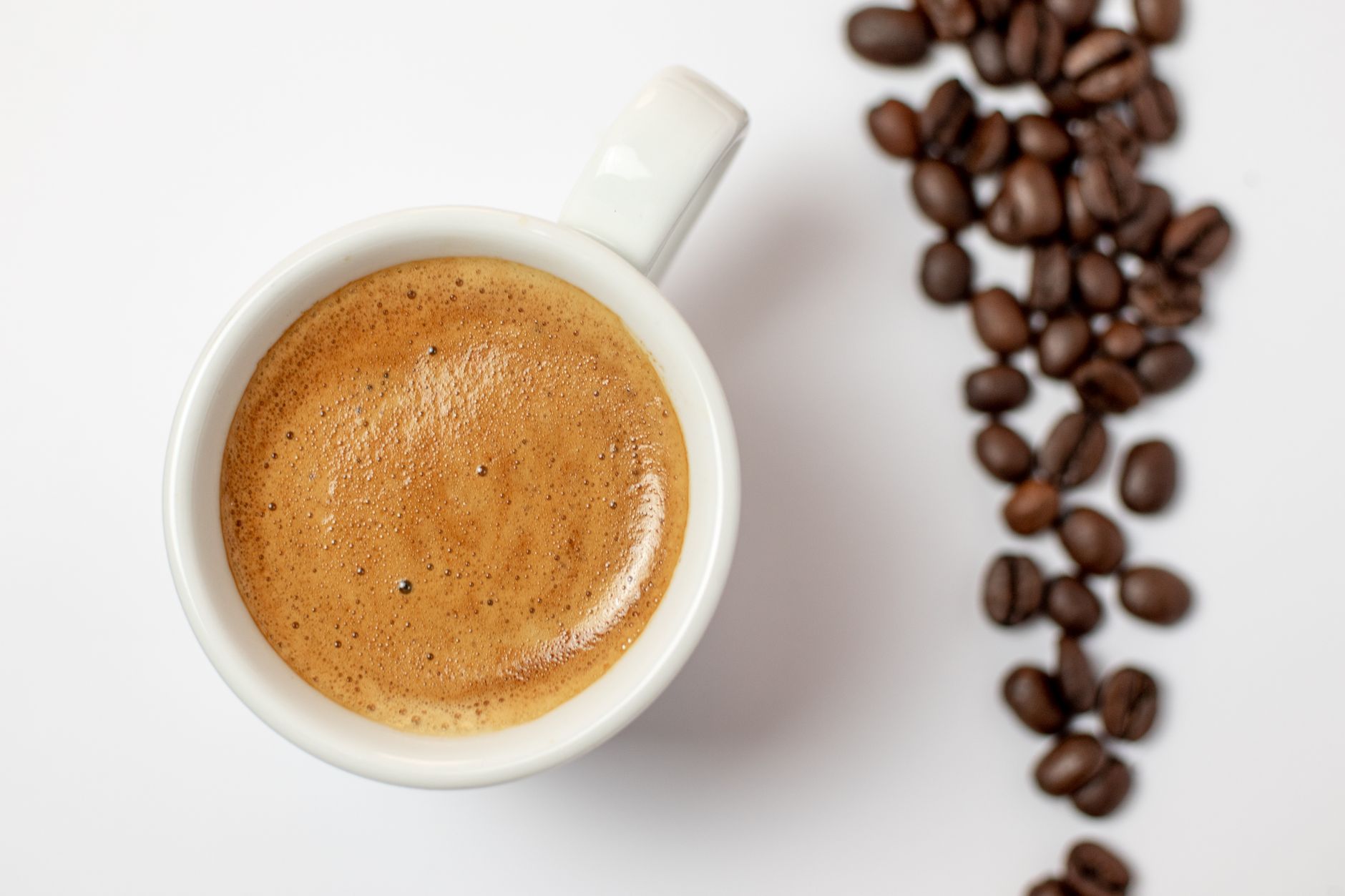 A warm cup of espresso with rich foam, served alongside scattered roasted coffee beans.