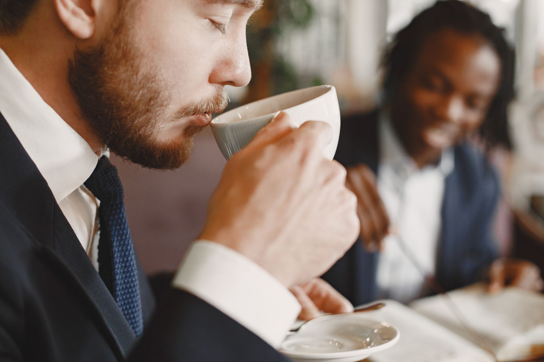 Two businessmen in formal attire enjoying coffee at a professional meeting.