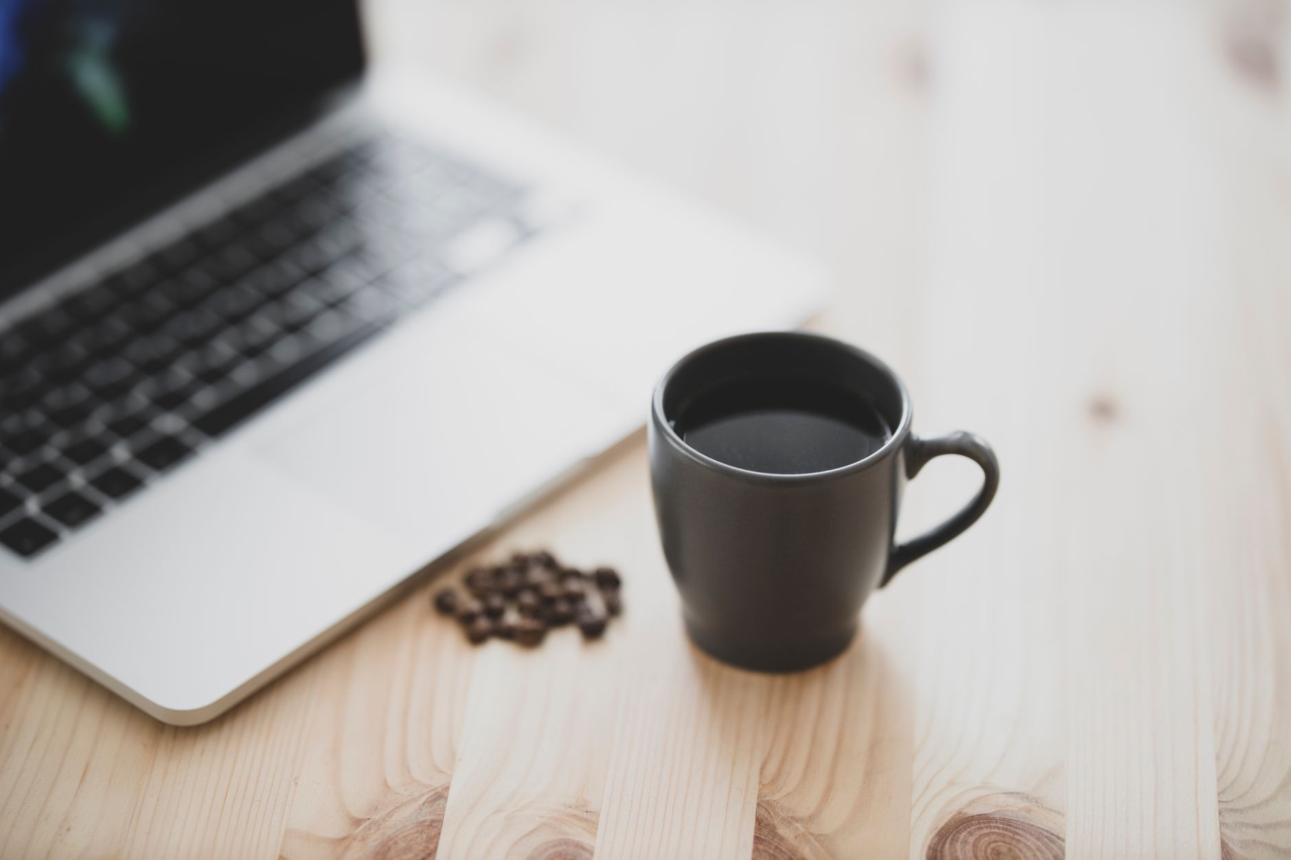 A close-up of a black coffee mug beside a laptop on a wooden table, creating a minimalist workspace vibe.