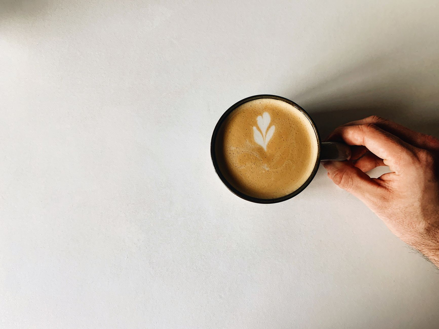 Top view of a latte with art held over a white surface. Minimalistic and calming.