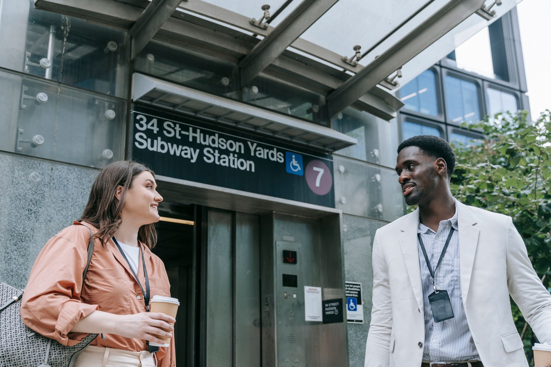 Two professionals conversing by 34th Street Hudson Yards Subway Station entrance in NYC.