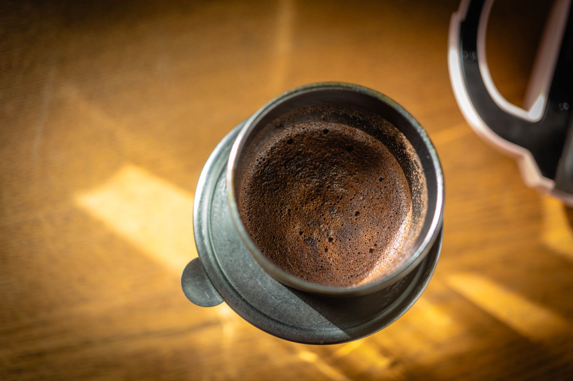 Overhead shot of fresh espresso with crema in a metallic mug on a sunlit wooden table.