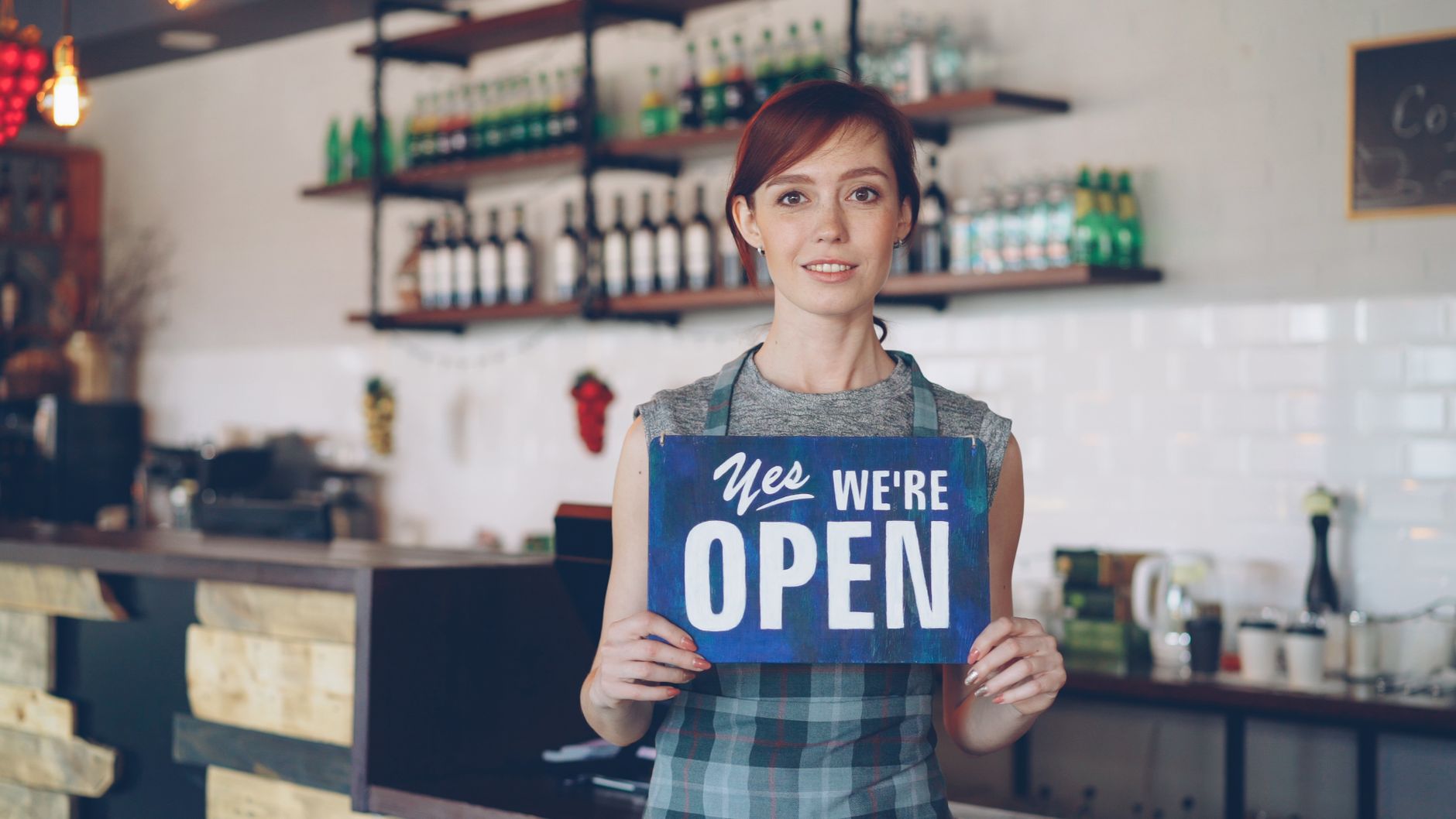 Young woman in cafe holding an open sign, welcoming customers.