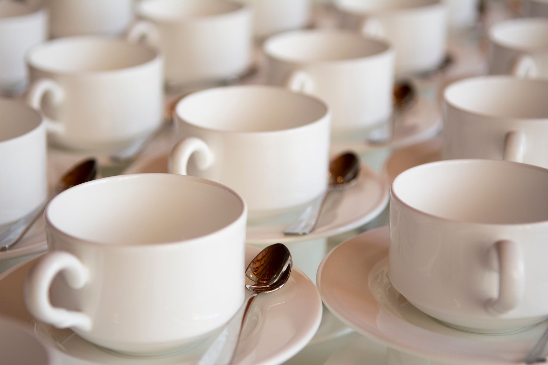 Close-up of elegant white porcelain coffee cups and saucers with spoons arranged in rows.