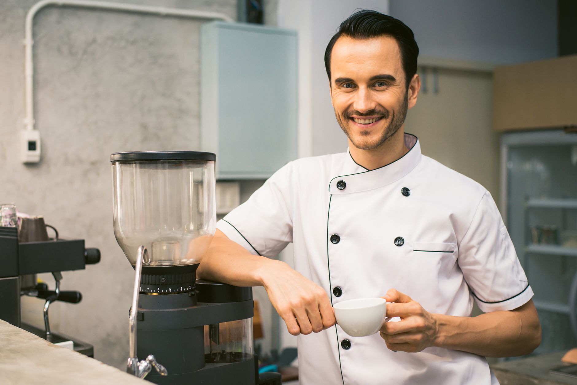 A cheerful barista in a coffee shop kitchen holding a coffee cup, ready to serve.