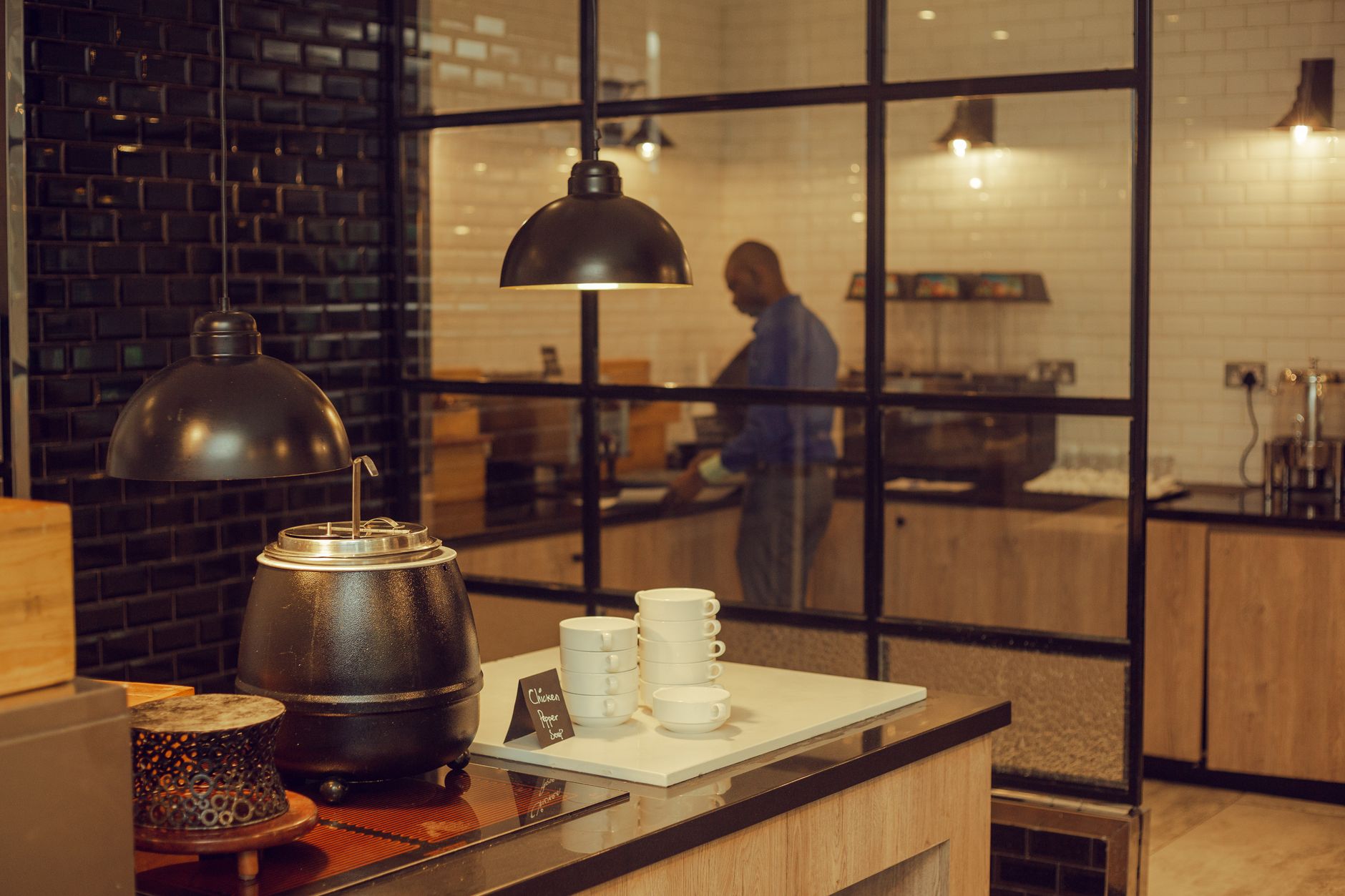 Stylish restaurant kitchen with soup pot, cups, and chef working in background.