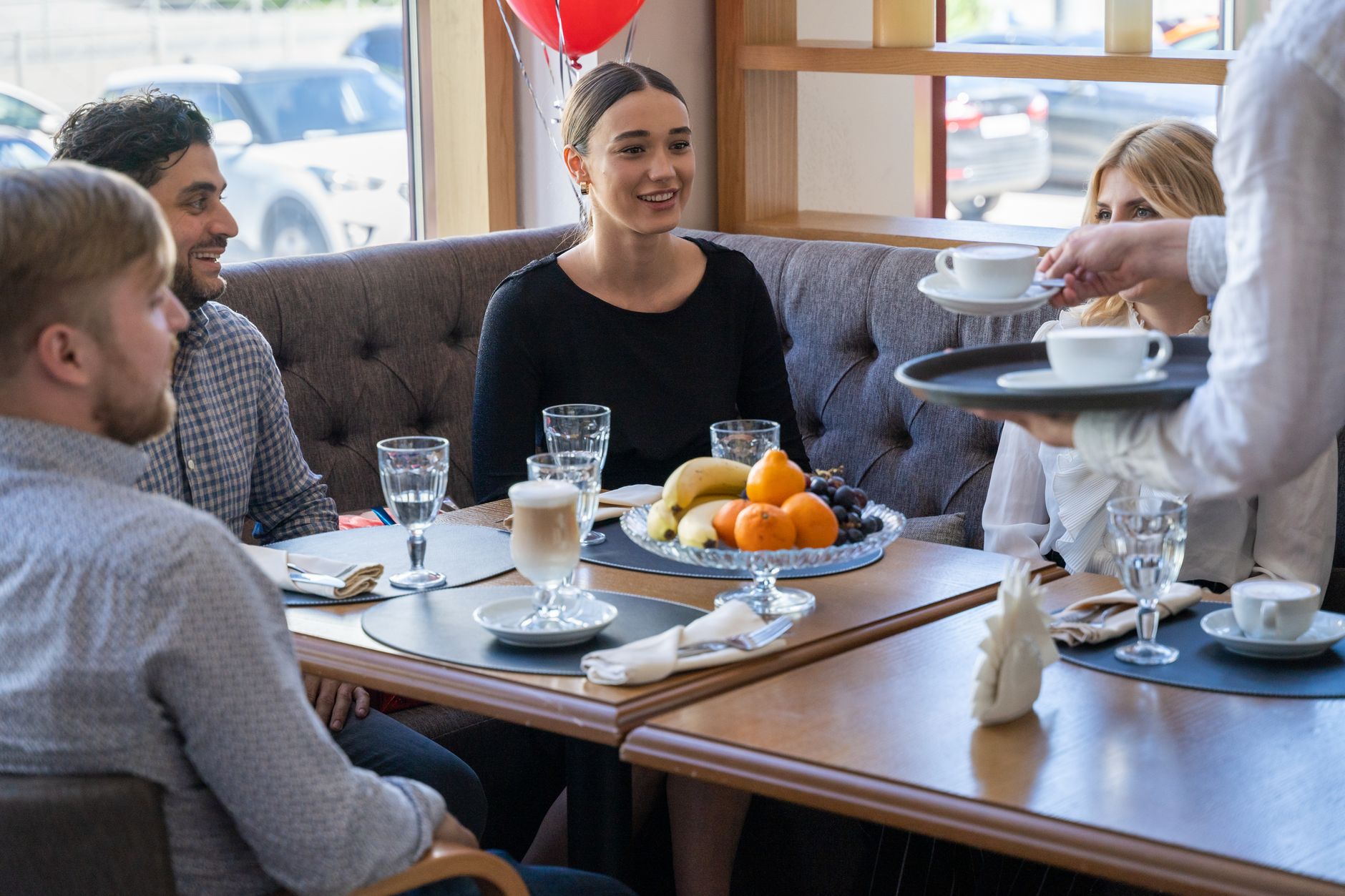 Four friends sitting indoors at a cafe enjoying coffee and conversation with a fruit platter in front of them.