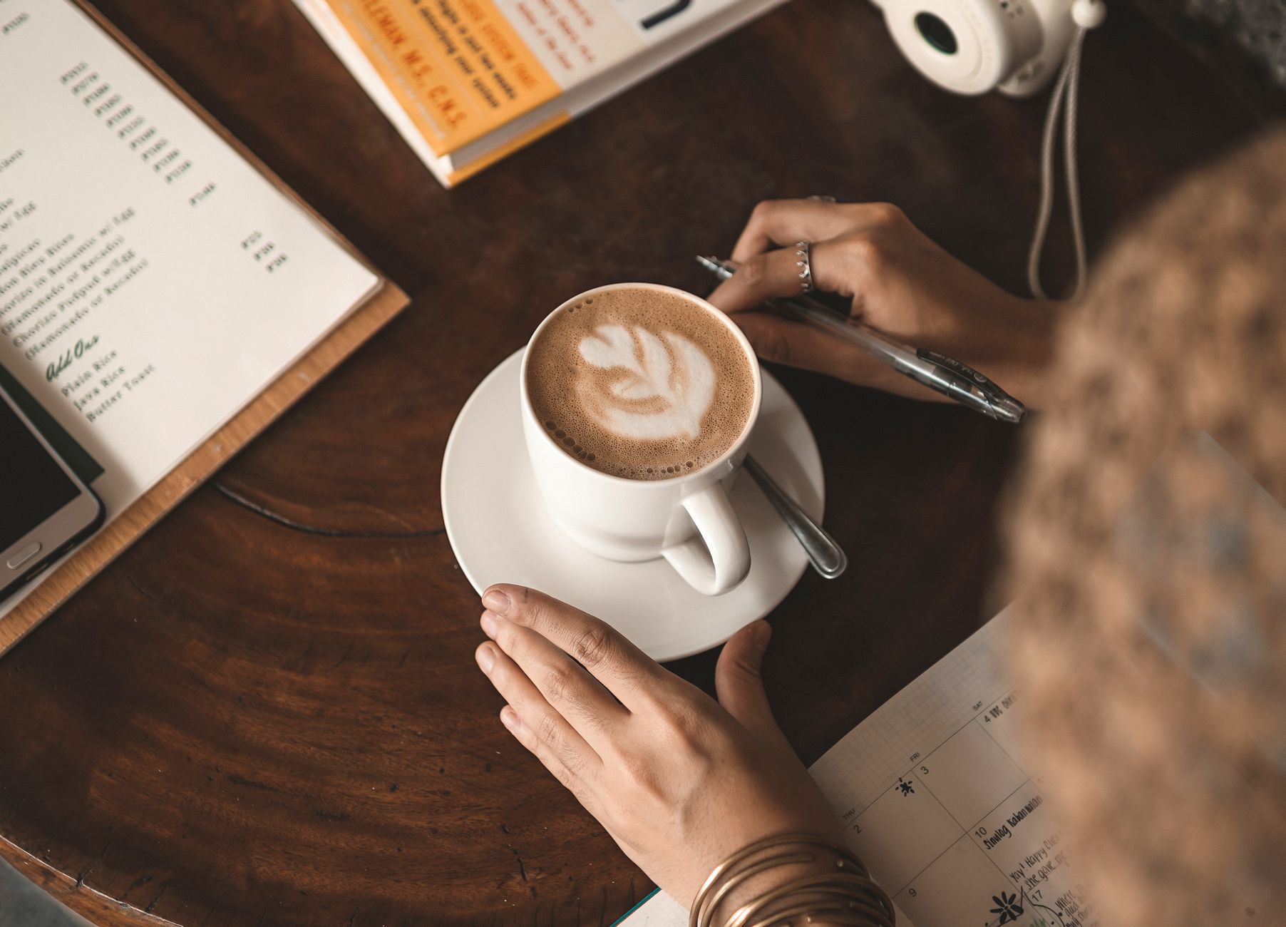 A woman enjoying a latte at a café while reviewing her planner. Warm and inviting.