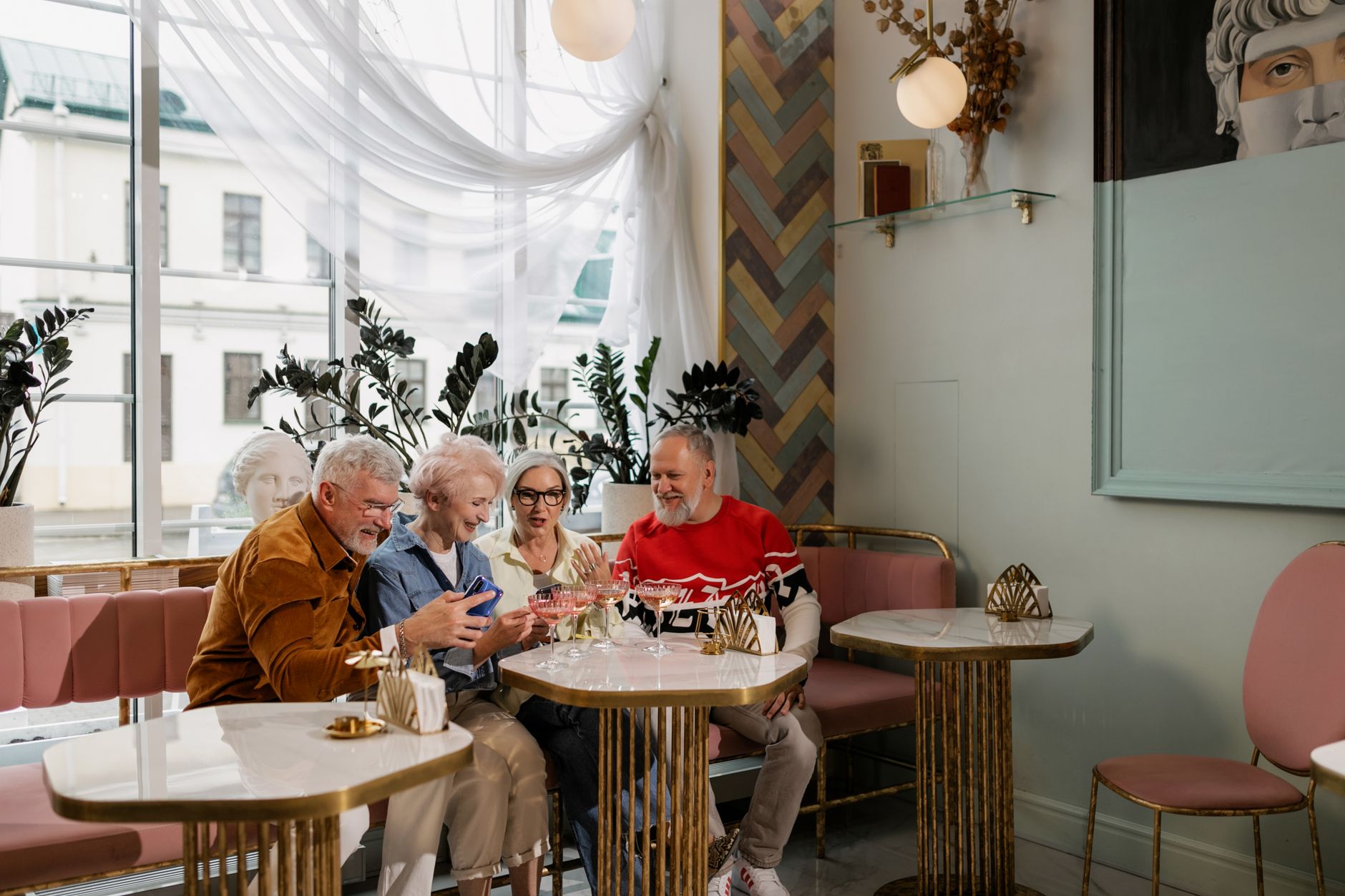 Elderly friends enjoying drinks and laughter in a charming indoor cafe setting.