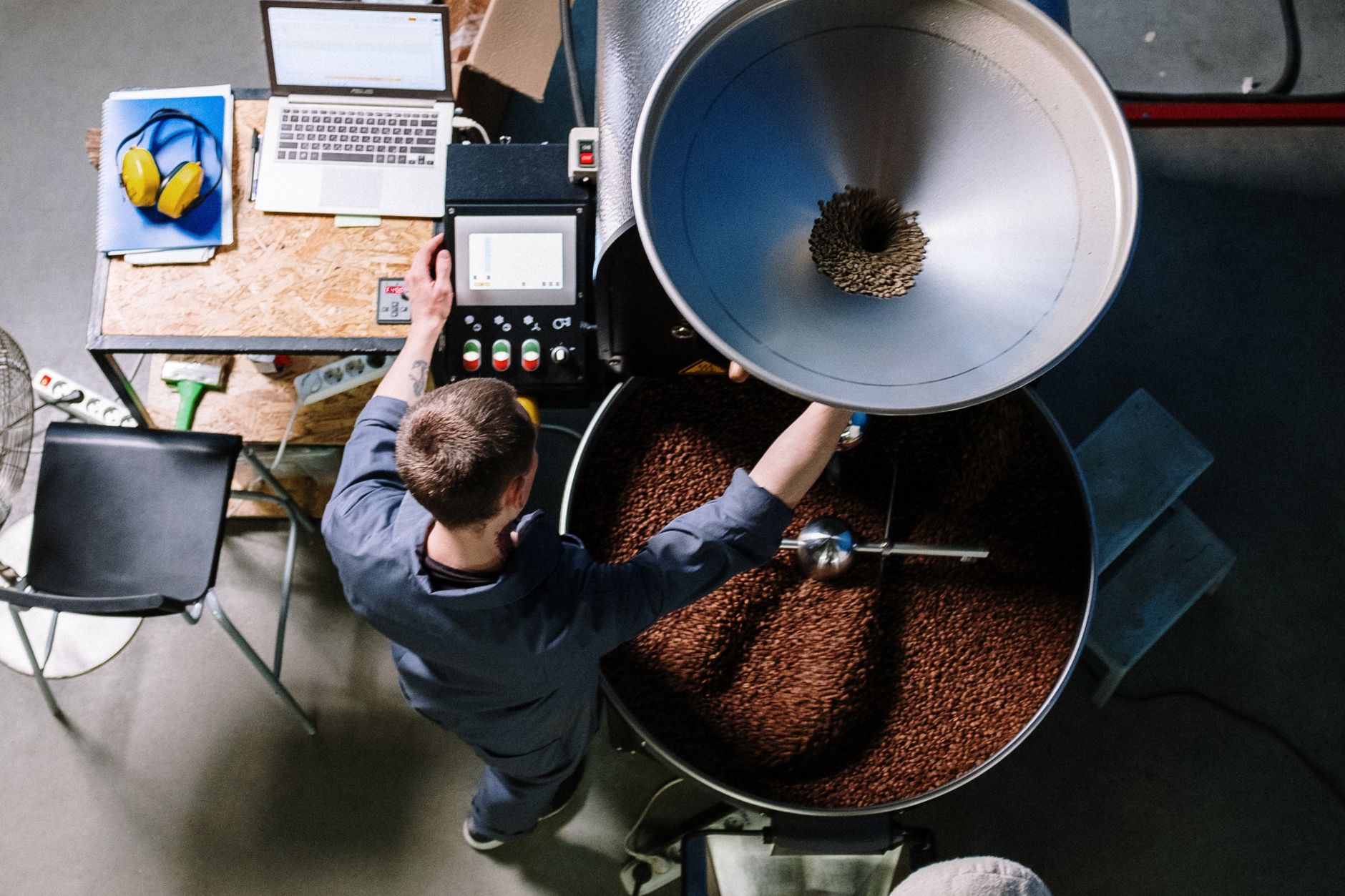 A worker in a coffee roastery operating equipment, processing fresh beans in an industrial setting.