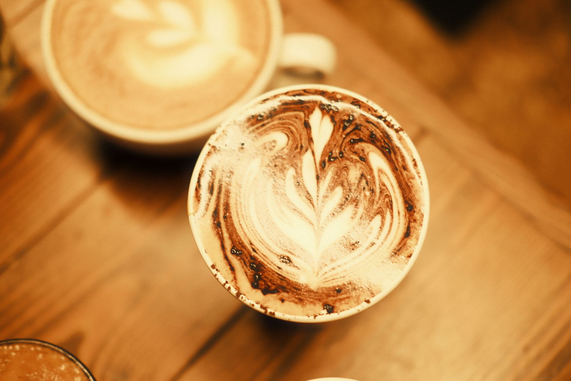Top view of cappuccinos with intricate latte art designs on a wooden table in a cozy cafe.