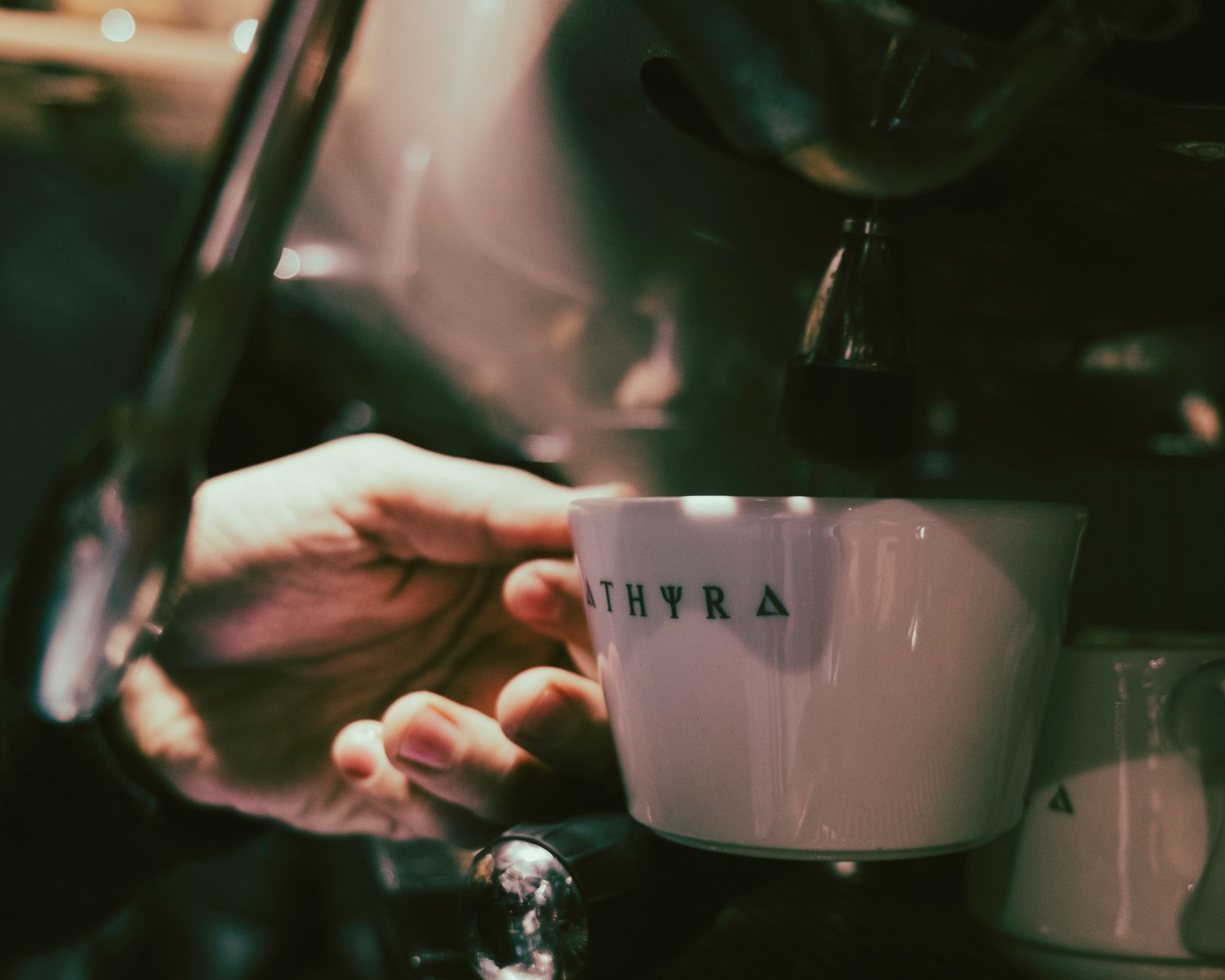 A barista holding a cup under an espresso machine spout, preparing coffee in a café setting.