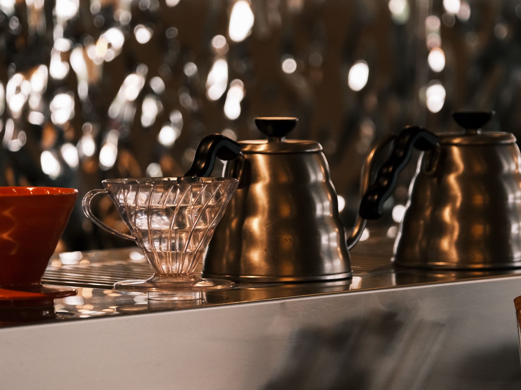 Close-up of stainless steel kettles and a coffee dripper at a modern coffee bar.