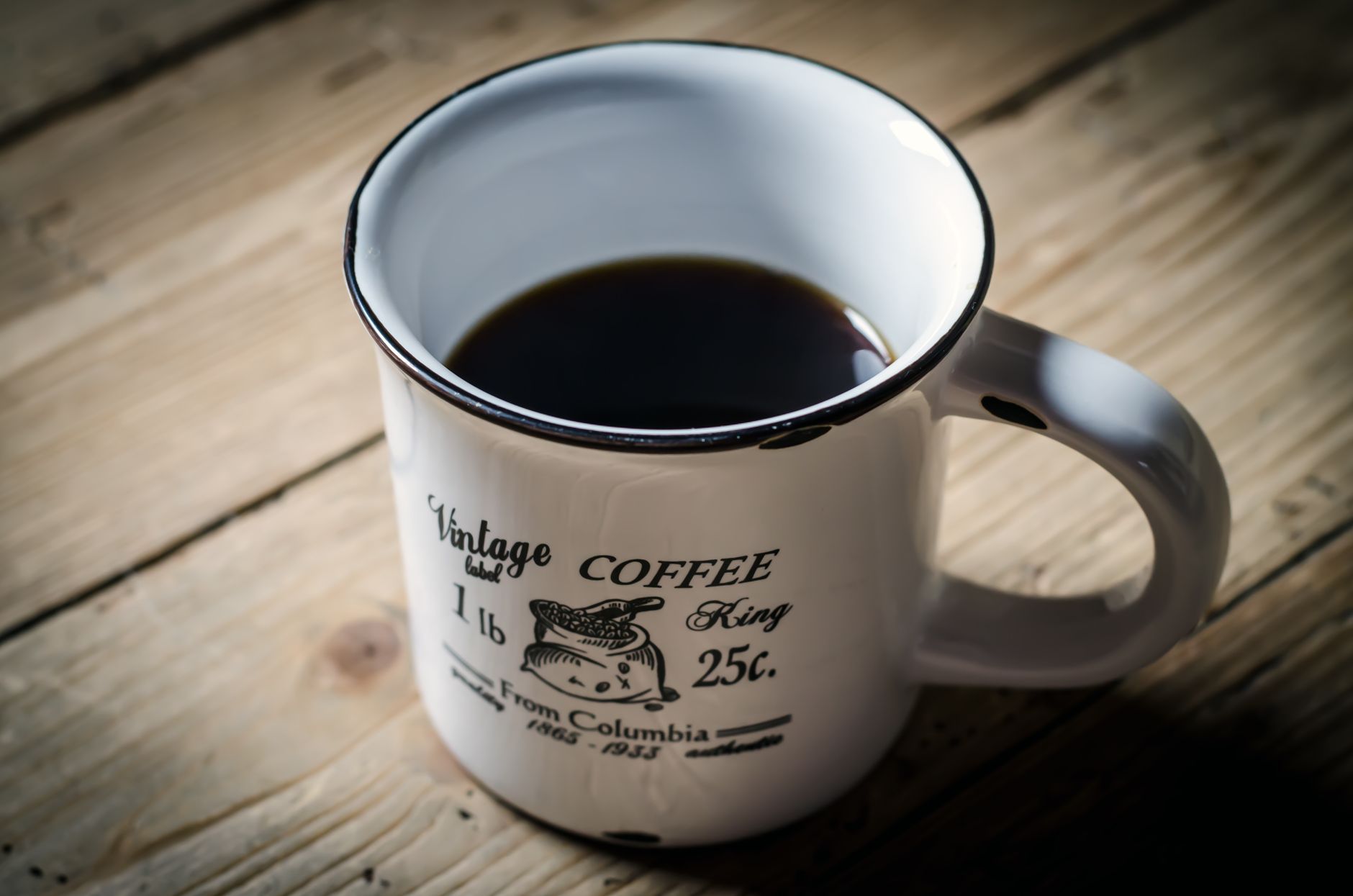 A vintage coffee mug with black coffee on a wooden table.