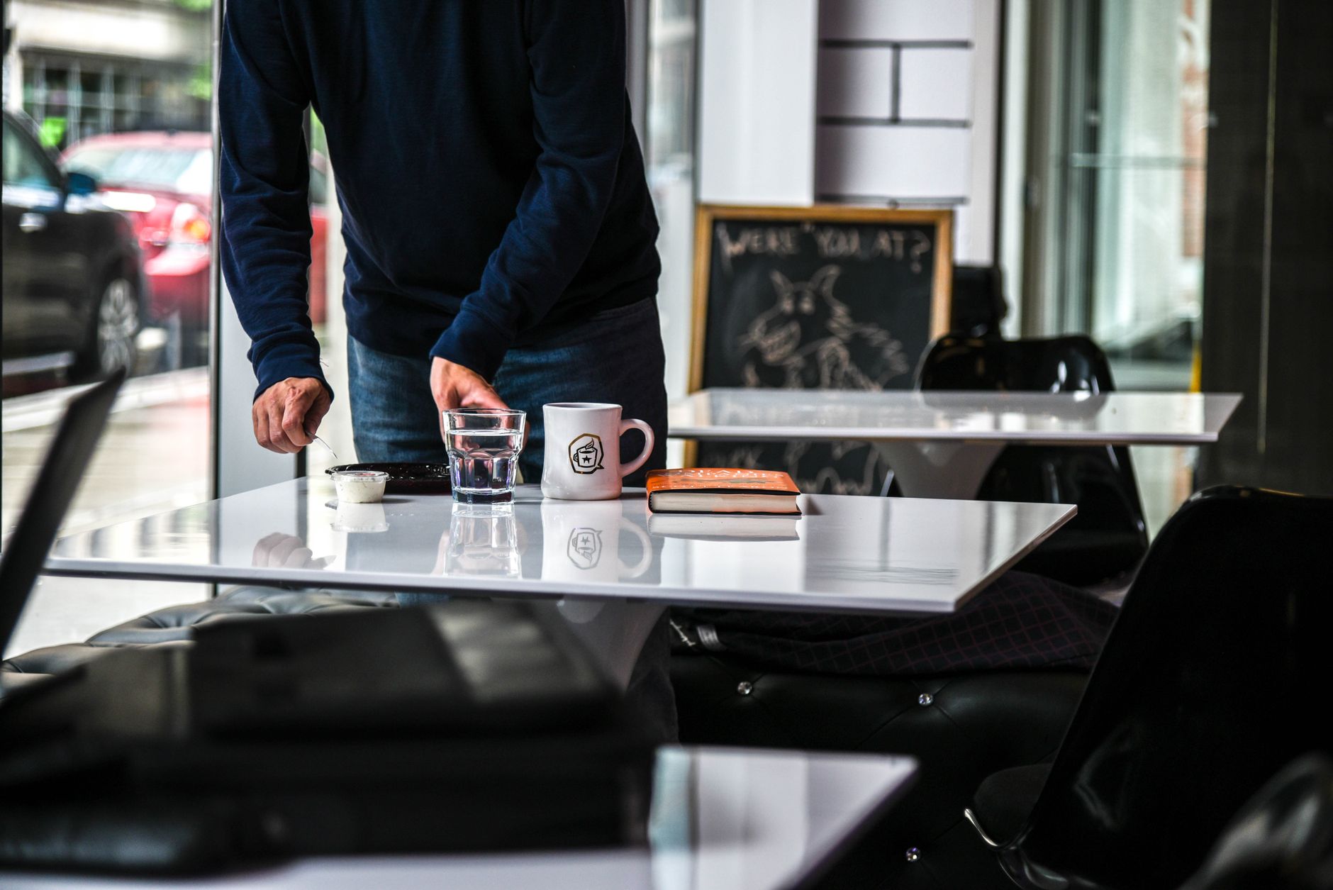 A person arranging a café table with a book, coffee, and glass indoors.