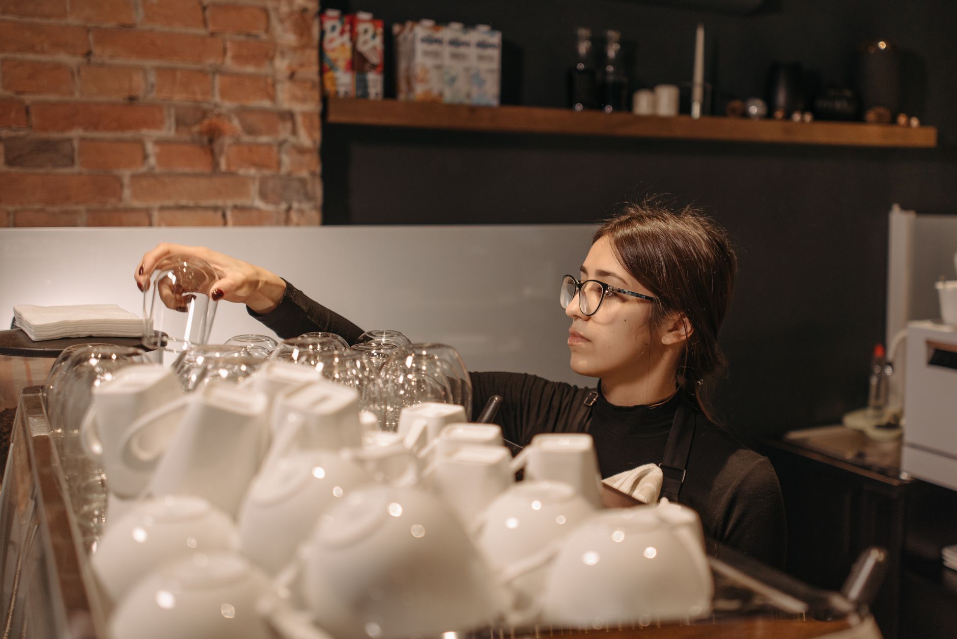 Female barista organizing cups in a warm, rustic coffee shop setting.