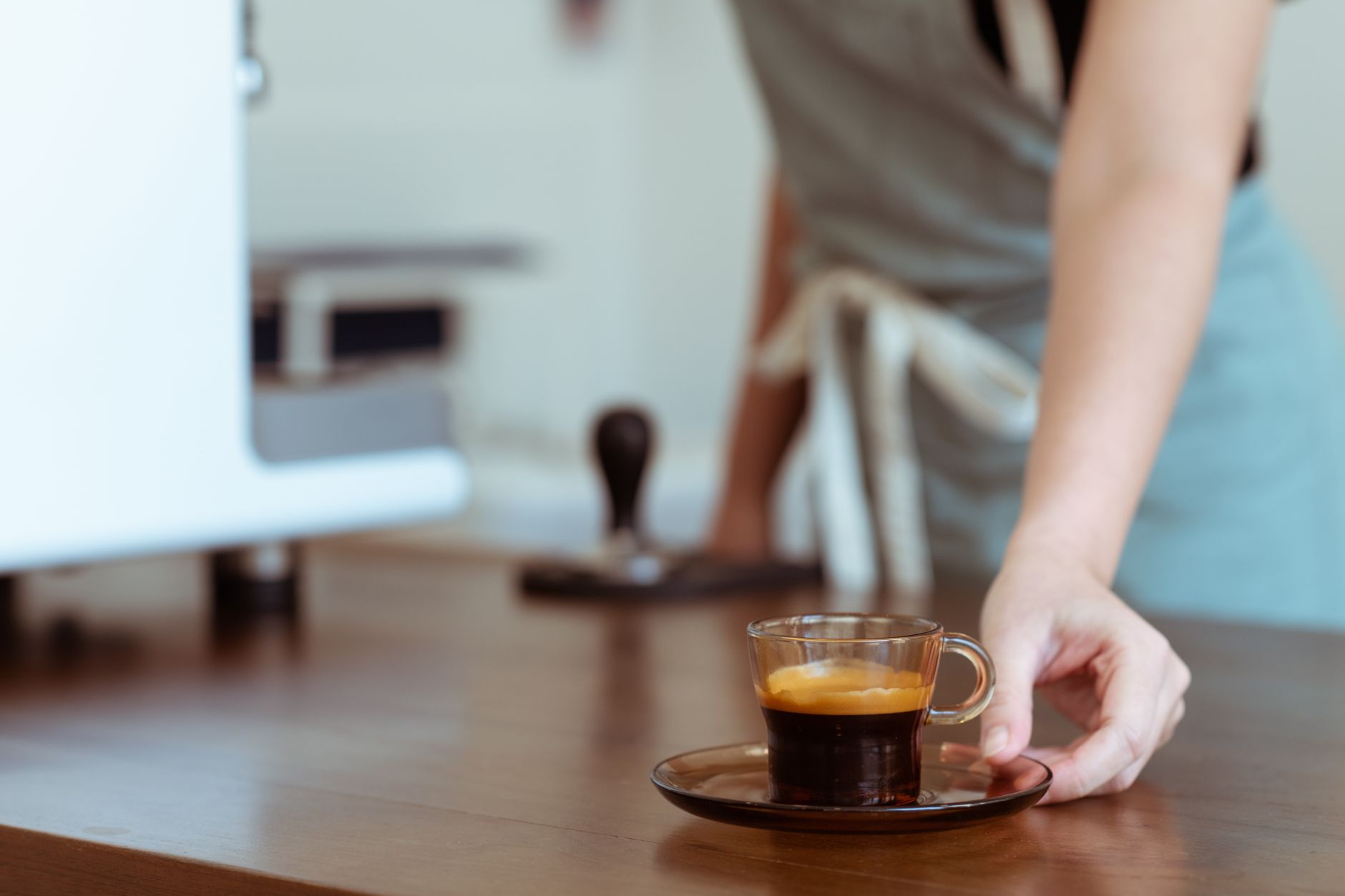 Crop faceless barista serving cup of fresh strong espresso in small glass cup on glass saucer