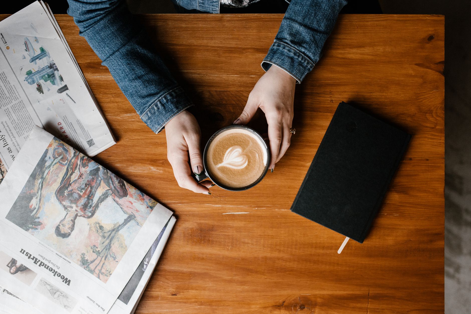 A cozy flat lay featuring a coffee cup, newspaper, and notebook on a wooden table.