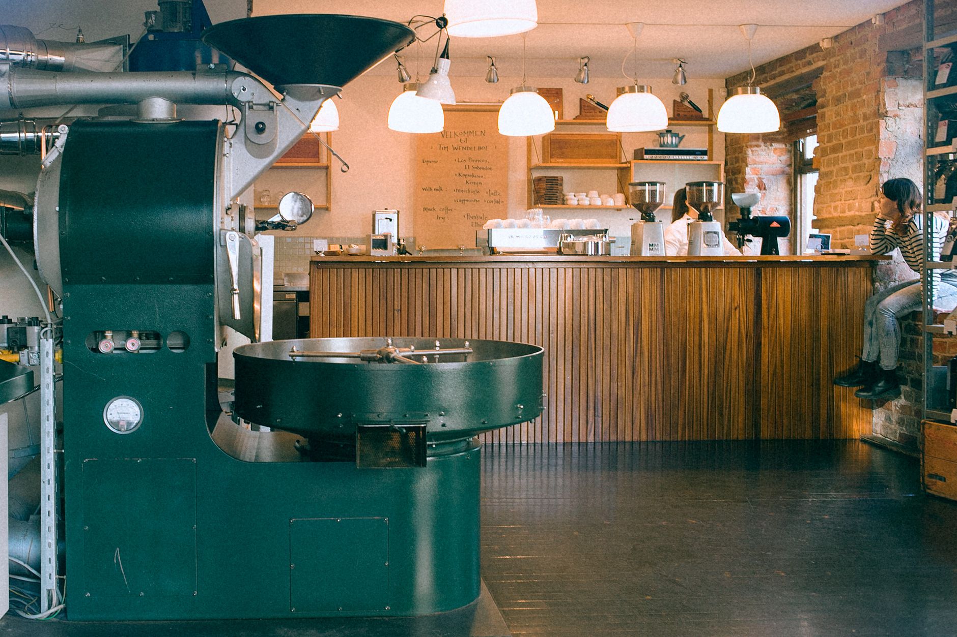 Coffee roasting equipment in cafeteria with lamps and crop unrecognizable female bartender with partner at work