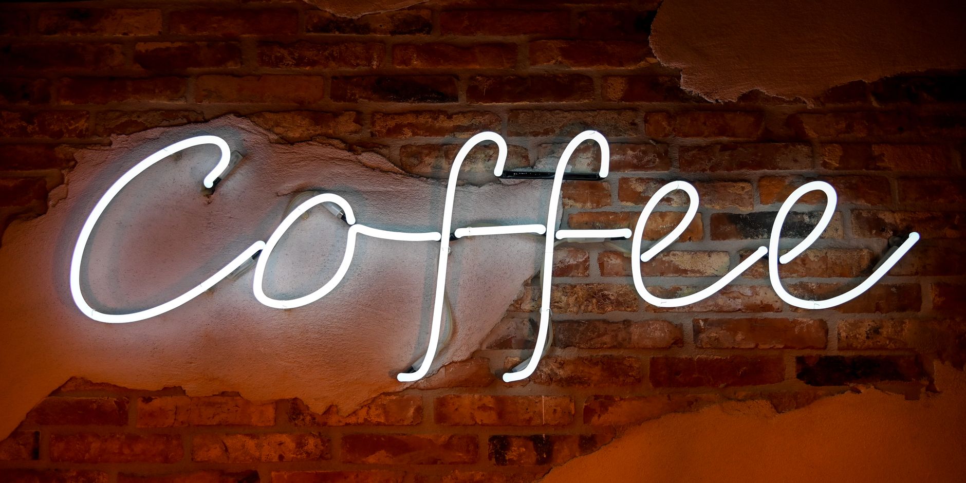 Glowing white neon coffee sign on rustic brick wall in cafe interior.