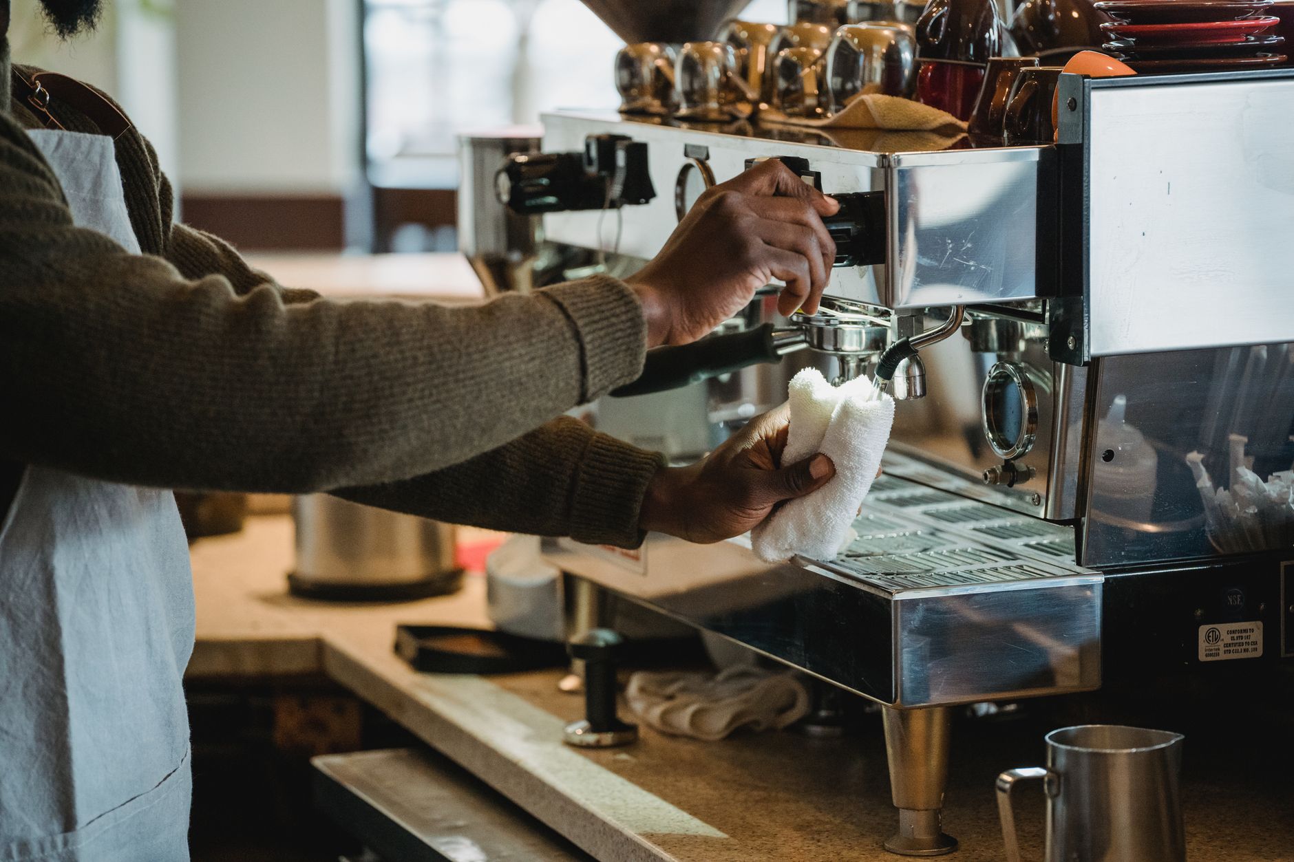 A barista cleans the coffee machine at a café, ensuring hygiene and readiness for customers.