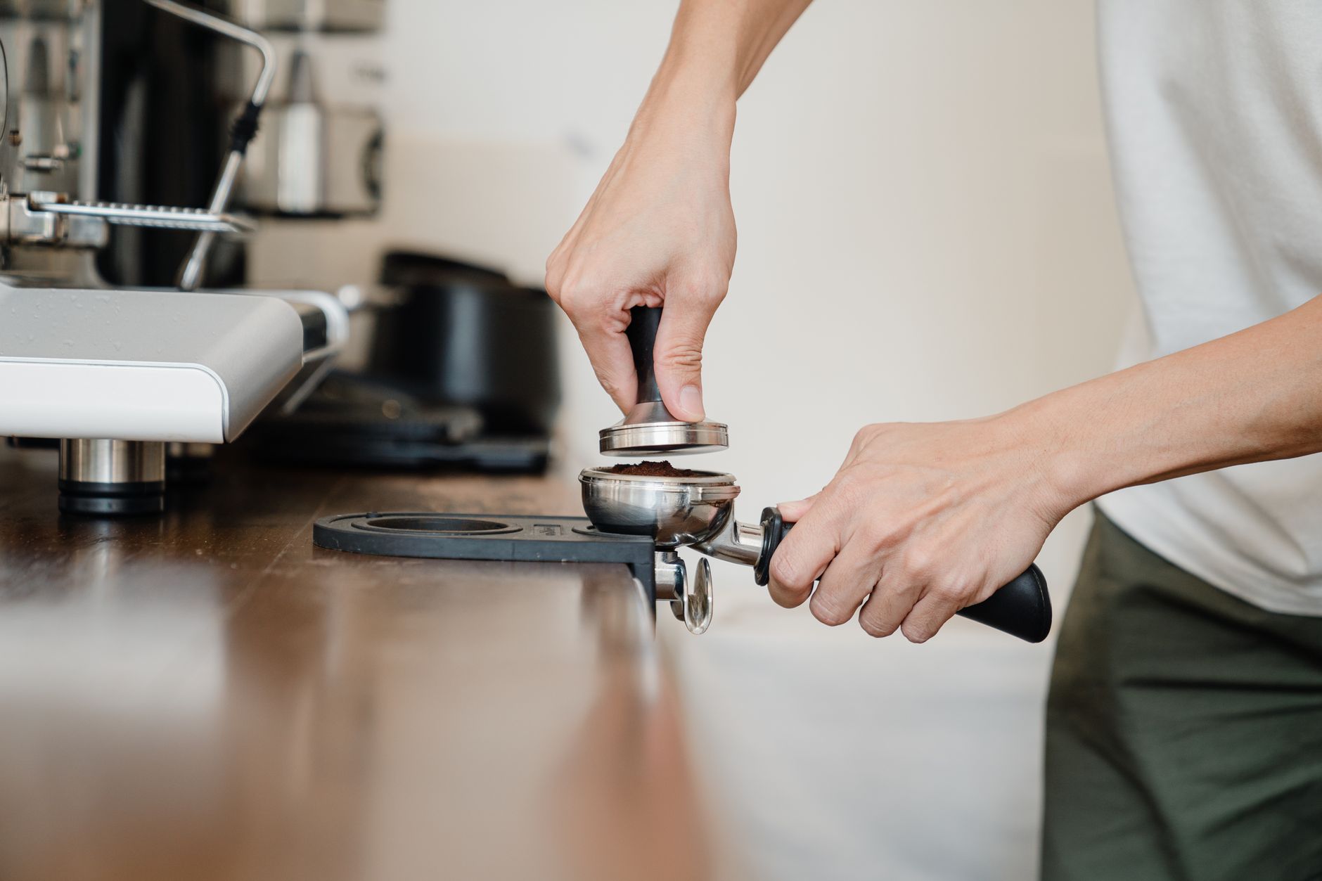 Close-up of barista hands using calibrated tamper and professional milk pitcher
