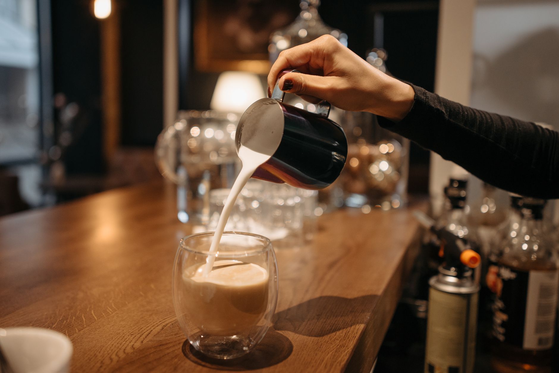 Professional barista pouring freshly brewed coffee from a reusable metal filter into a carafe in a commercial kitchen