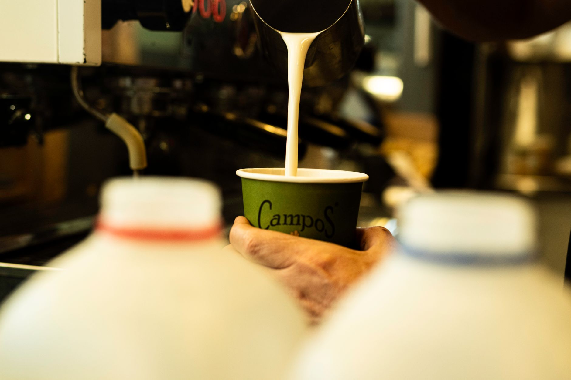 Professional barista pouring intricate latte art design in busy cafe