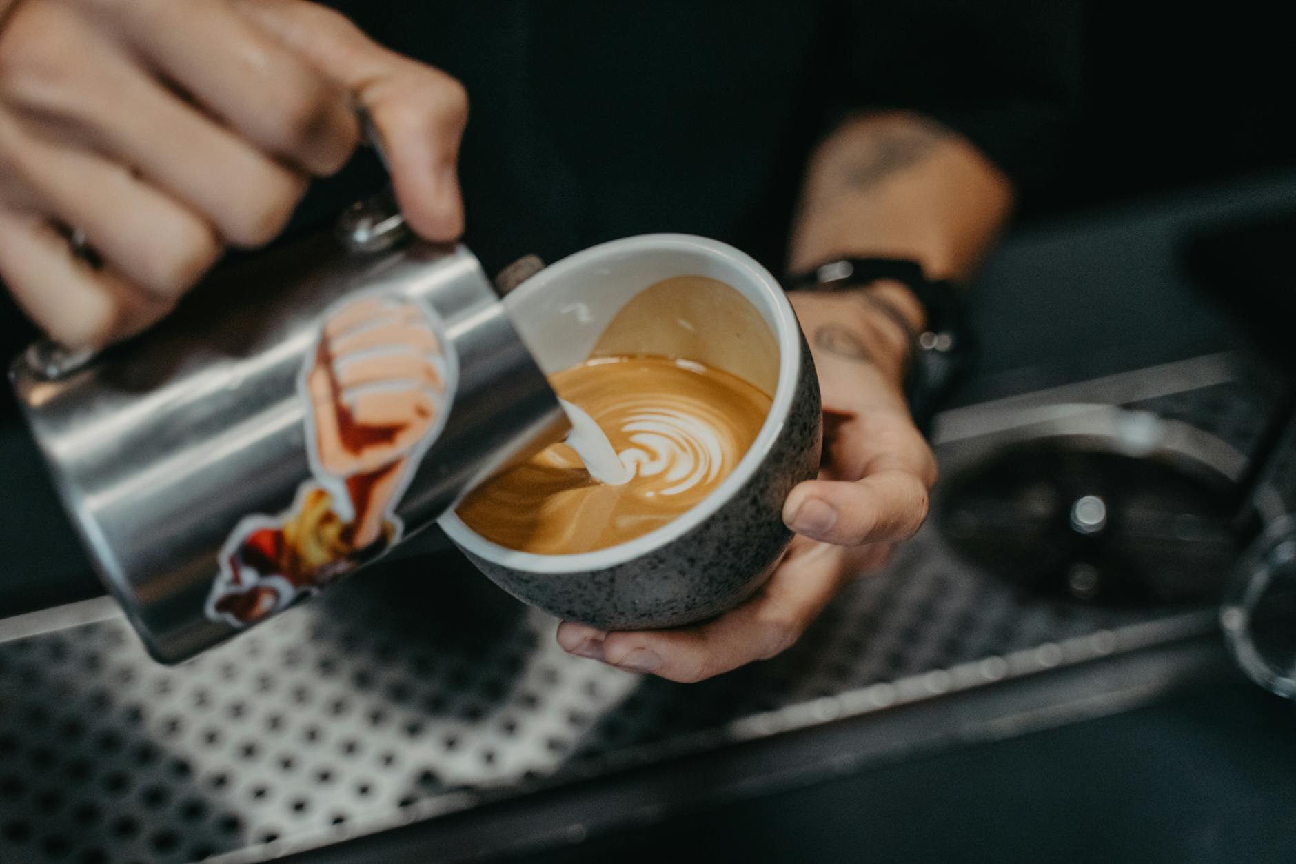 Barista pouring latte art heart into a ceramic cup using a stainless steel pitcher