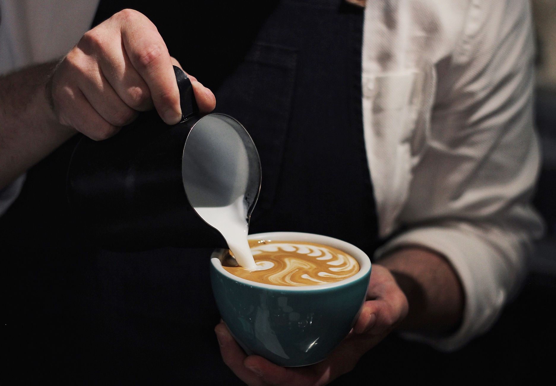 Professional barista deep cleaning milk pitcher and steaming wand