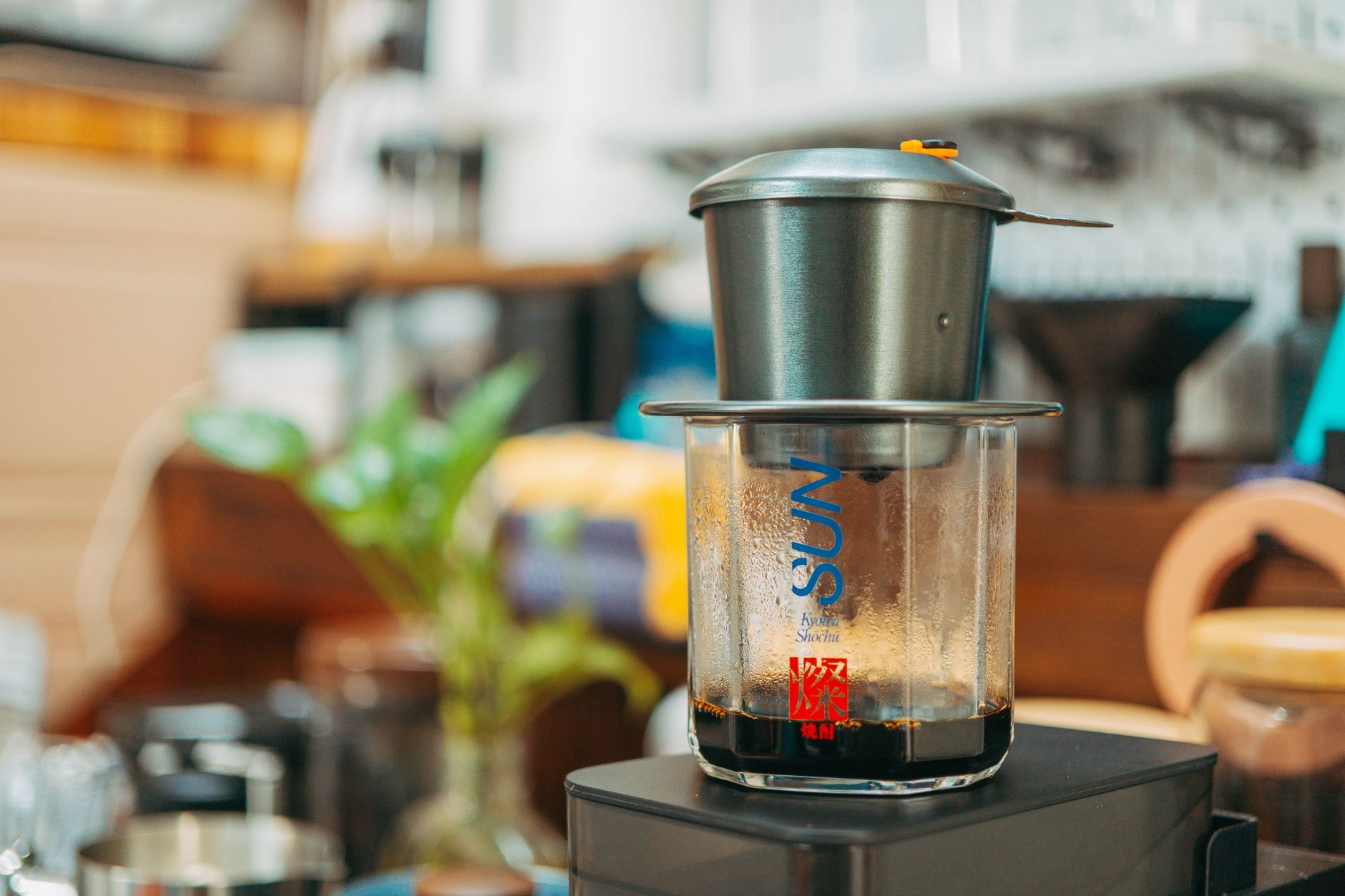 Close-up of a Vietnamese coffee drip filter brewing in a cozy kitchen interior with blurred background.